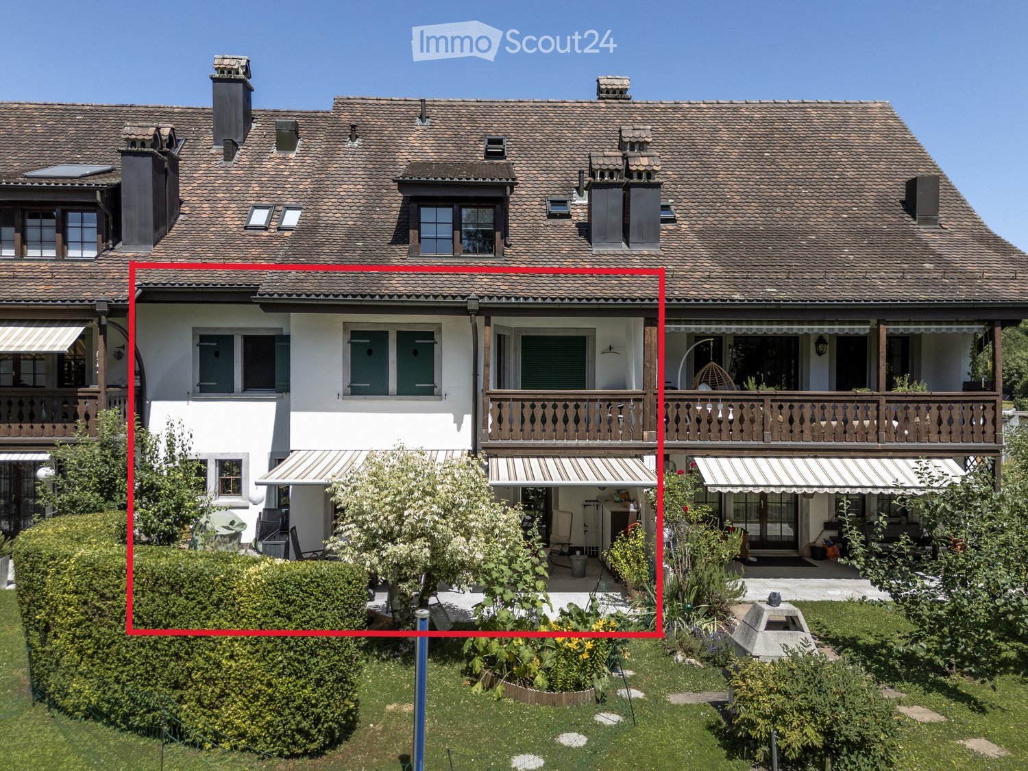 2 story house, brown roof, brown trim, awnings, small front garden, plants, hedge, balcony, outdoor seating area