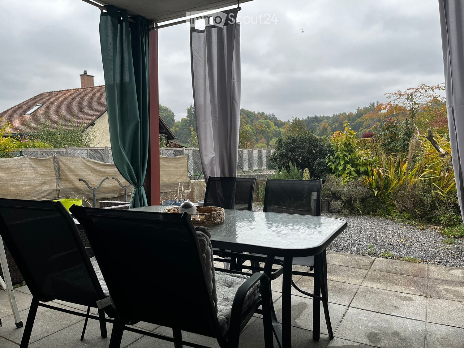 table, chairs, covered with curtains, view of the house, garden, and trees