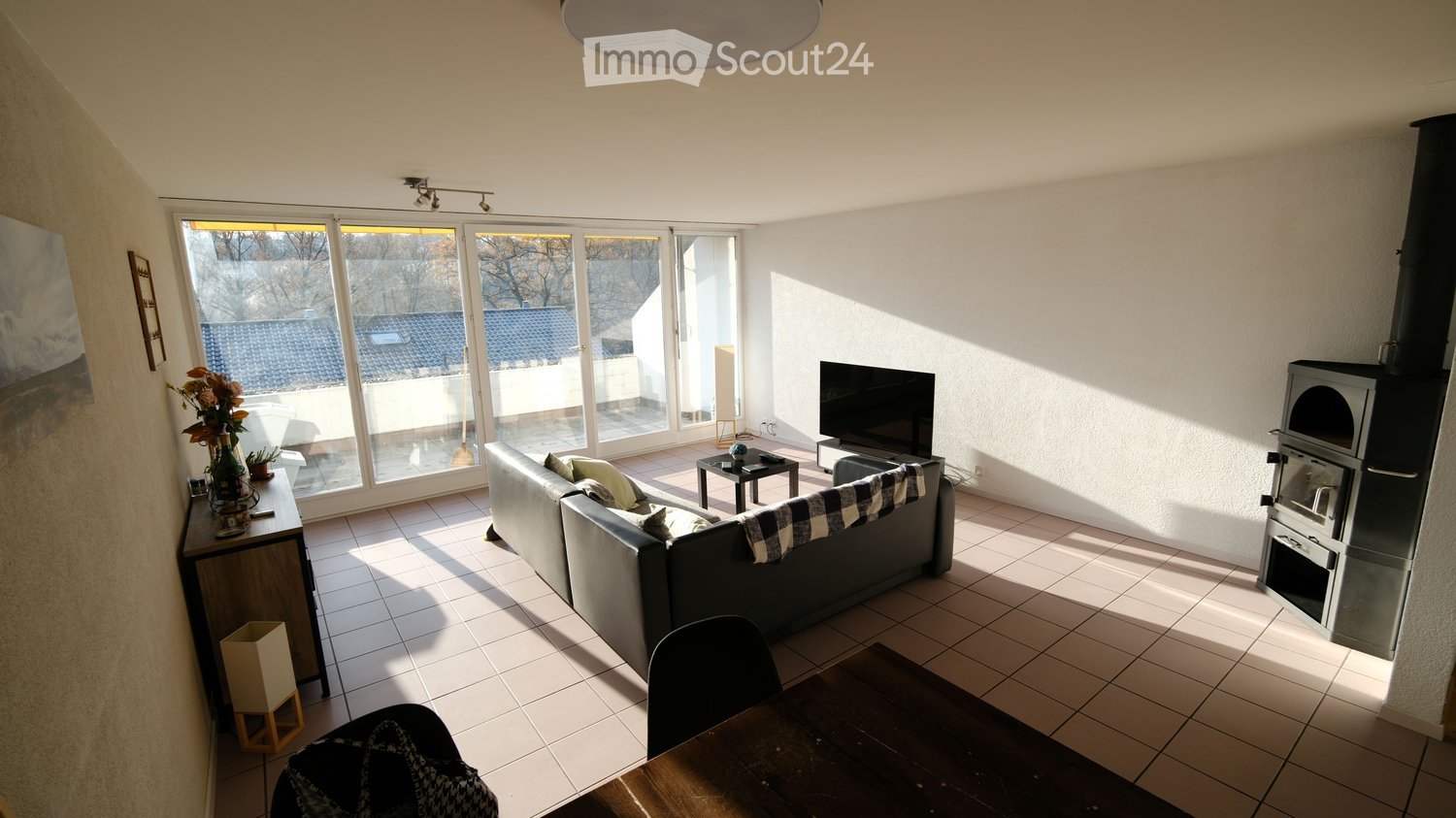 black couch, flat screen TV, glass sliding doors leading to balcony, fireplace, tile floor, table, paintings on wall