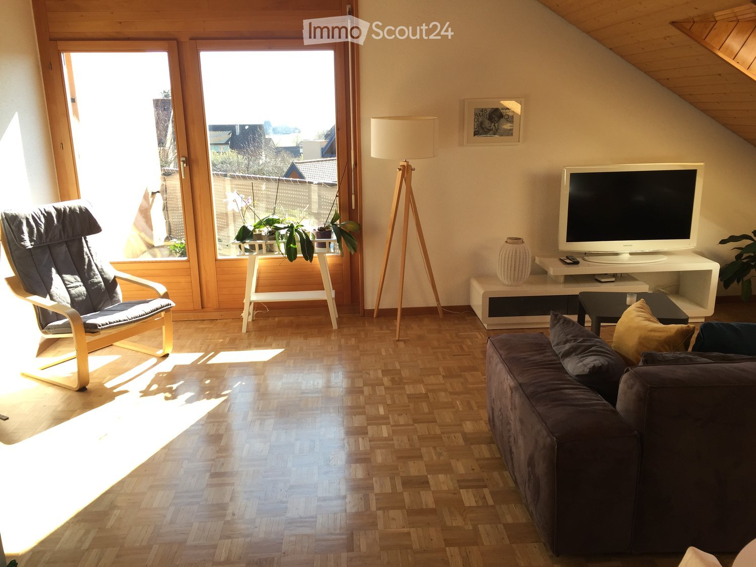 Spacious living room with large windows, wooden flooring, white walls, couch, tv, chair, and a floor lamp