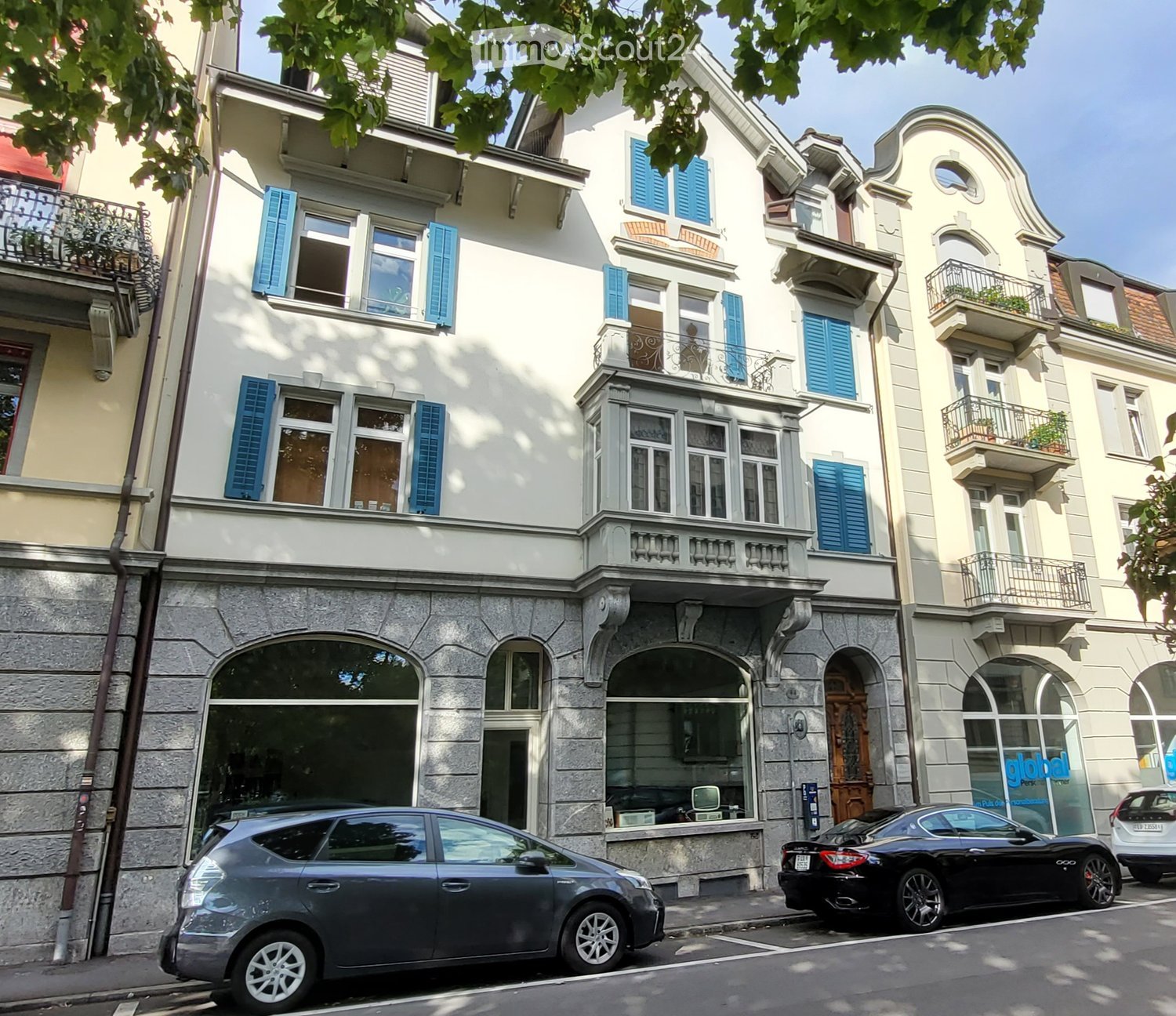 3 story building, white exterior, blue shutters, balconies, arched windows, storefronts, cars parked in front