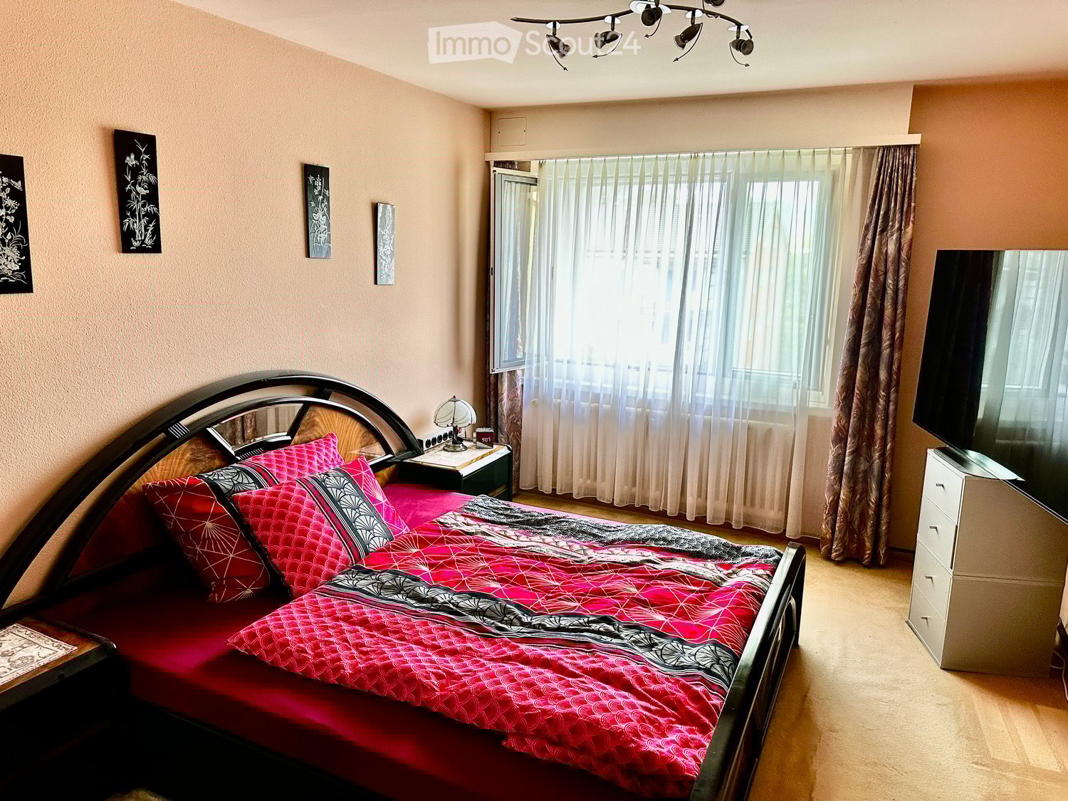 a large bed with multiple pillows, nightstand with lamp, a television on the dresser