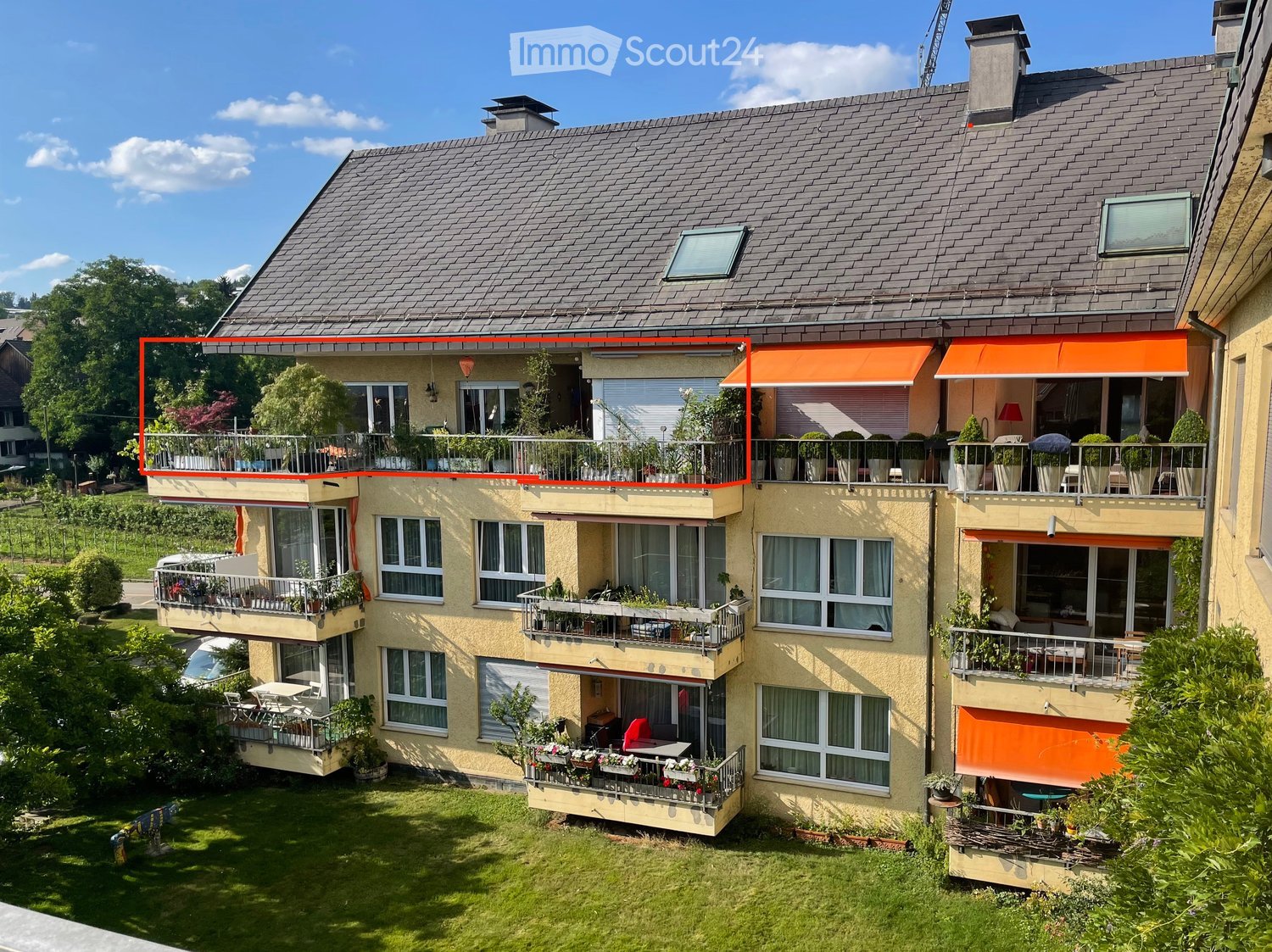 Multi-story apartment building with balconies, orange awnings, and a grassy area in front