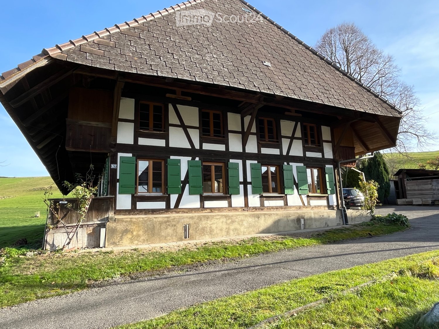 Traditional house, brown roof, green shutters, stone and white walls, green lawn, rural setting