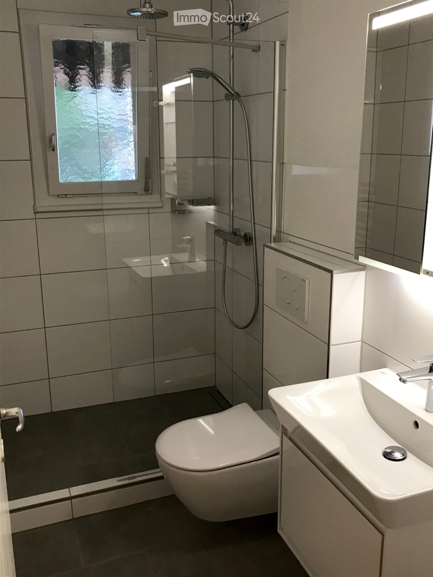 Small bathroom with a shower, a sink, and a toilet. Tiled walls, silver fittings, white fixtures.