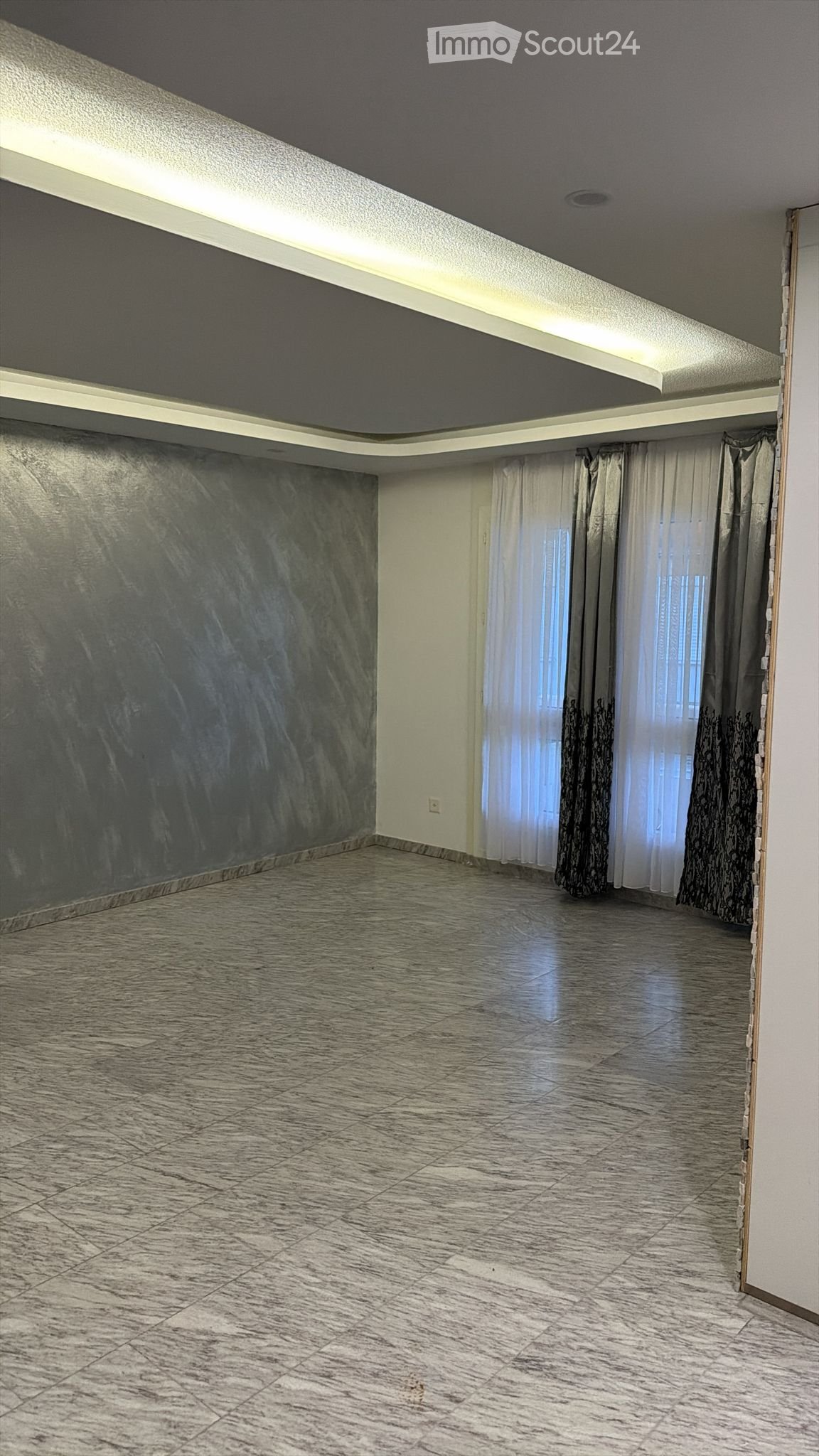 Empty room, tiled floor, gray walls, long white curtains with black designs, light strip on ceiling.