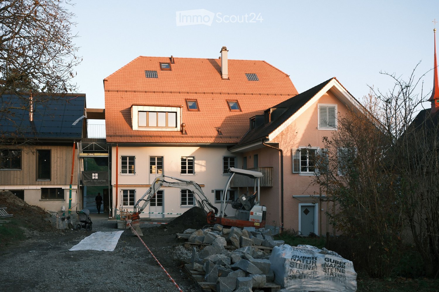 2-story house, orange roof, white walls, solar panels, window sills, door, construction machinery, pile of stones