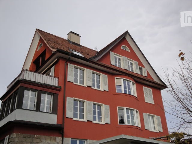 Multistory building, red facade, white shutters, gable roof, chimney, multiple windows, balcony on the first floor