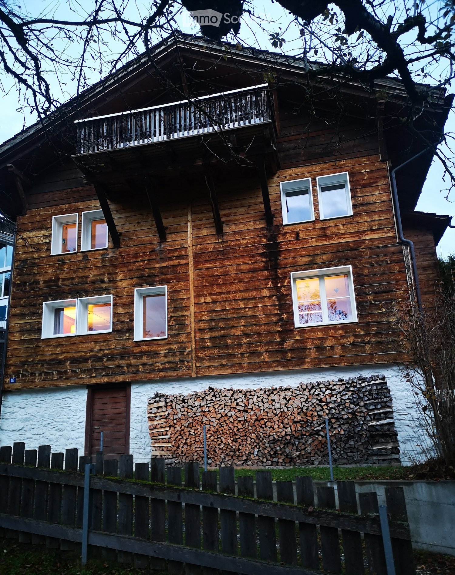 wooden exterior house, wooden balcony, several windows, pile of wood for firewood