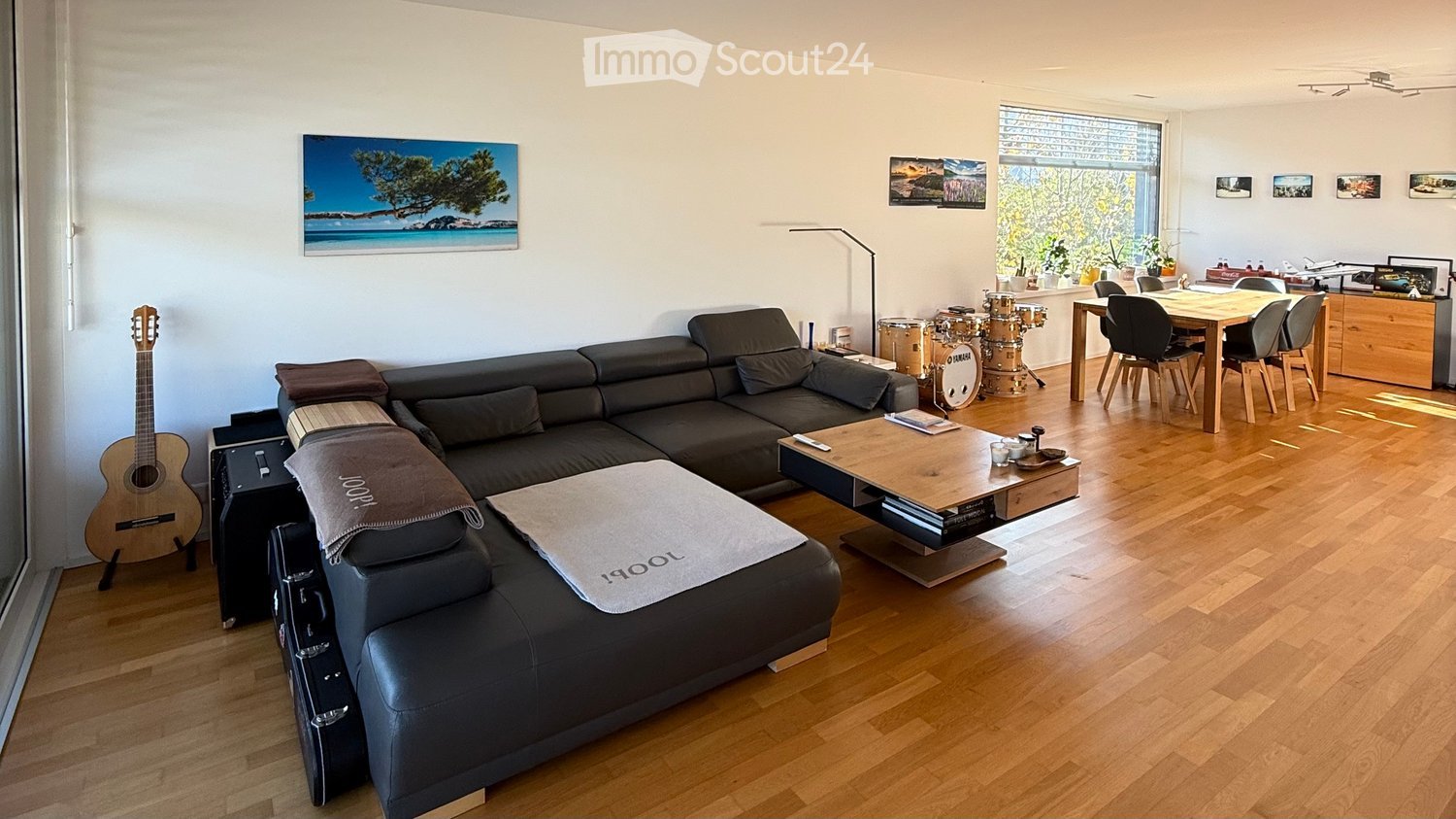 L-shaped black leather couch, wooden coffee table, wooden dining table, acoustic guitar, glass window, picture frames