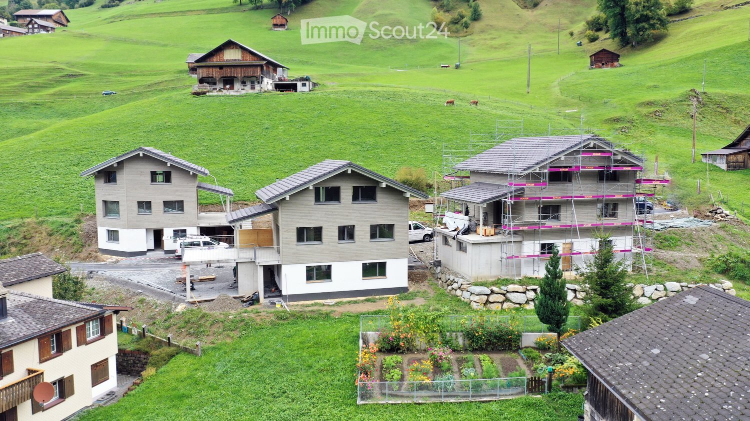 Four residential houses, some under construction, located in a hilly area with green meadows, houses have various construction stages.