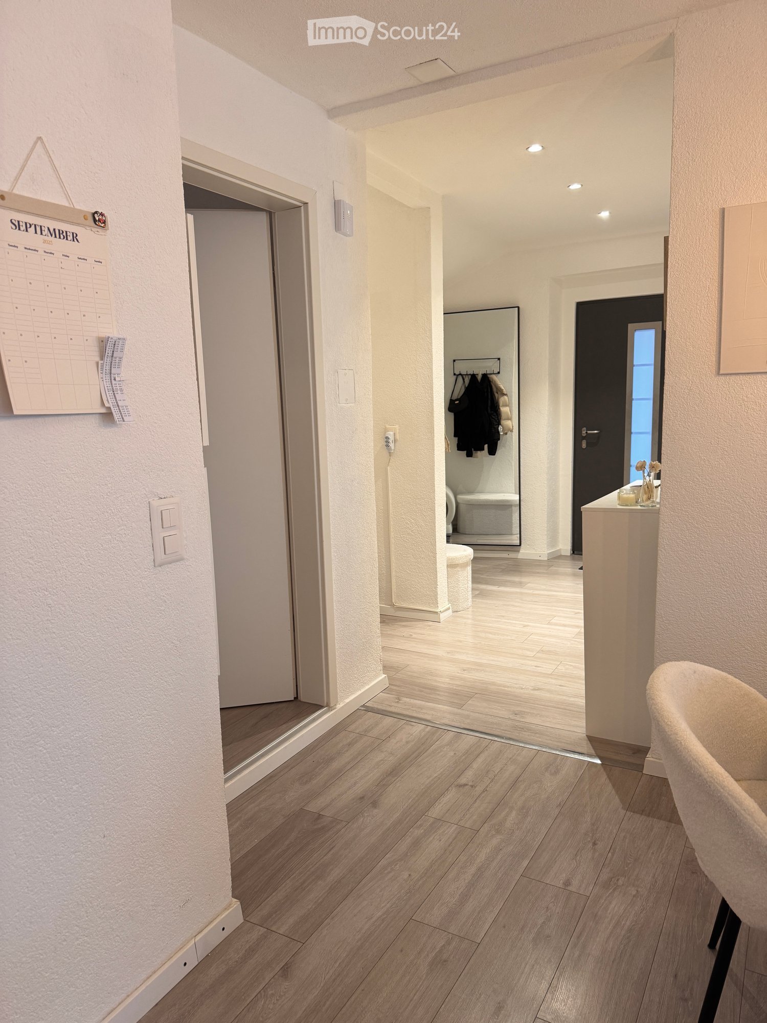 long hallway with white walls, wooden floor, and a white chair on the right
