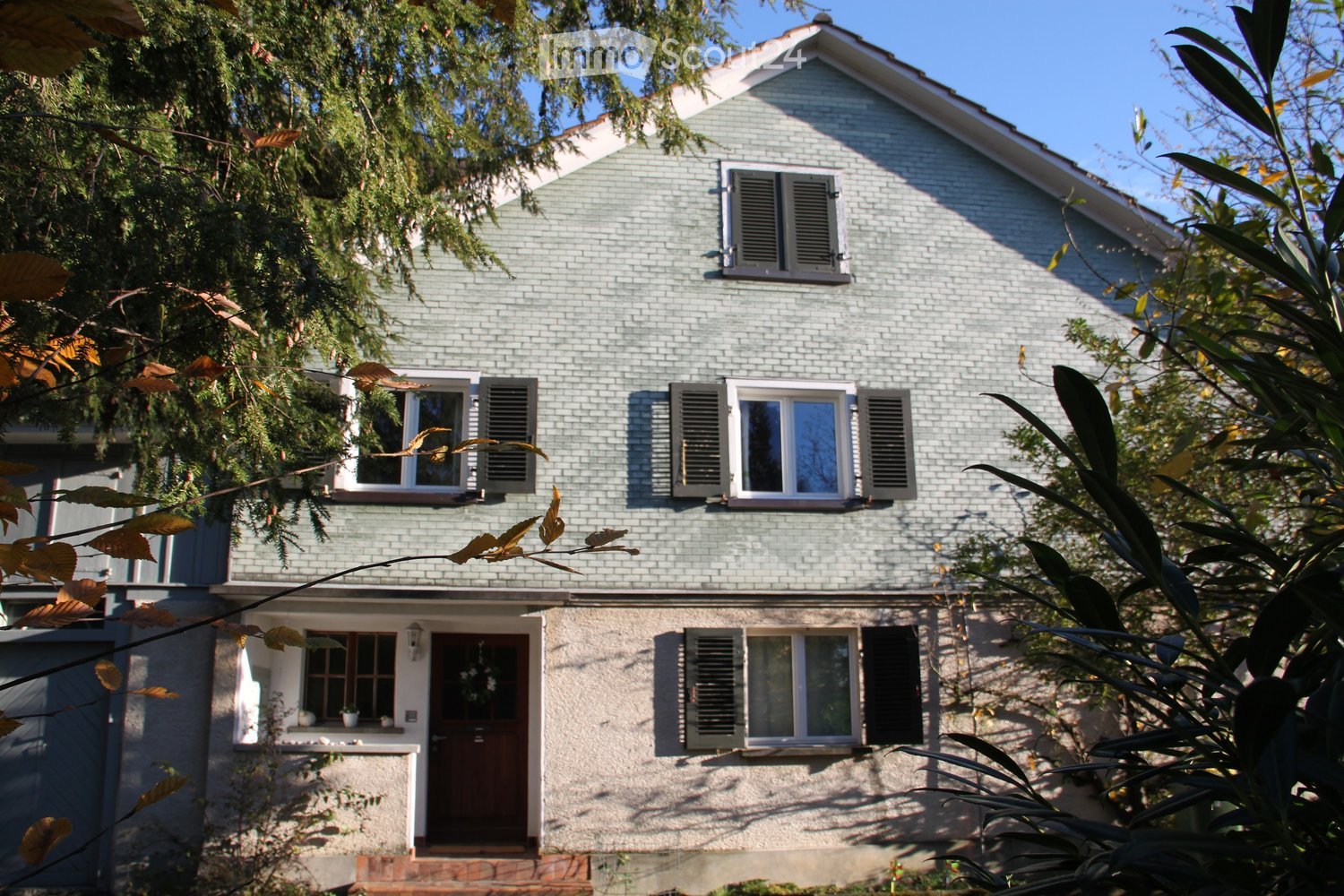 2-story house, brick walls, white windows with shutters, wooden front door, located in a tree-lined street.