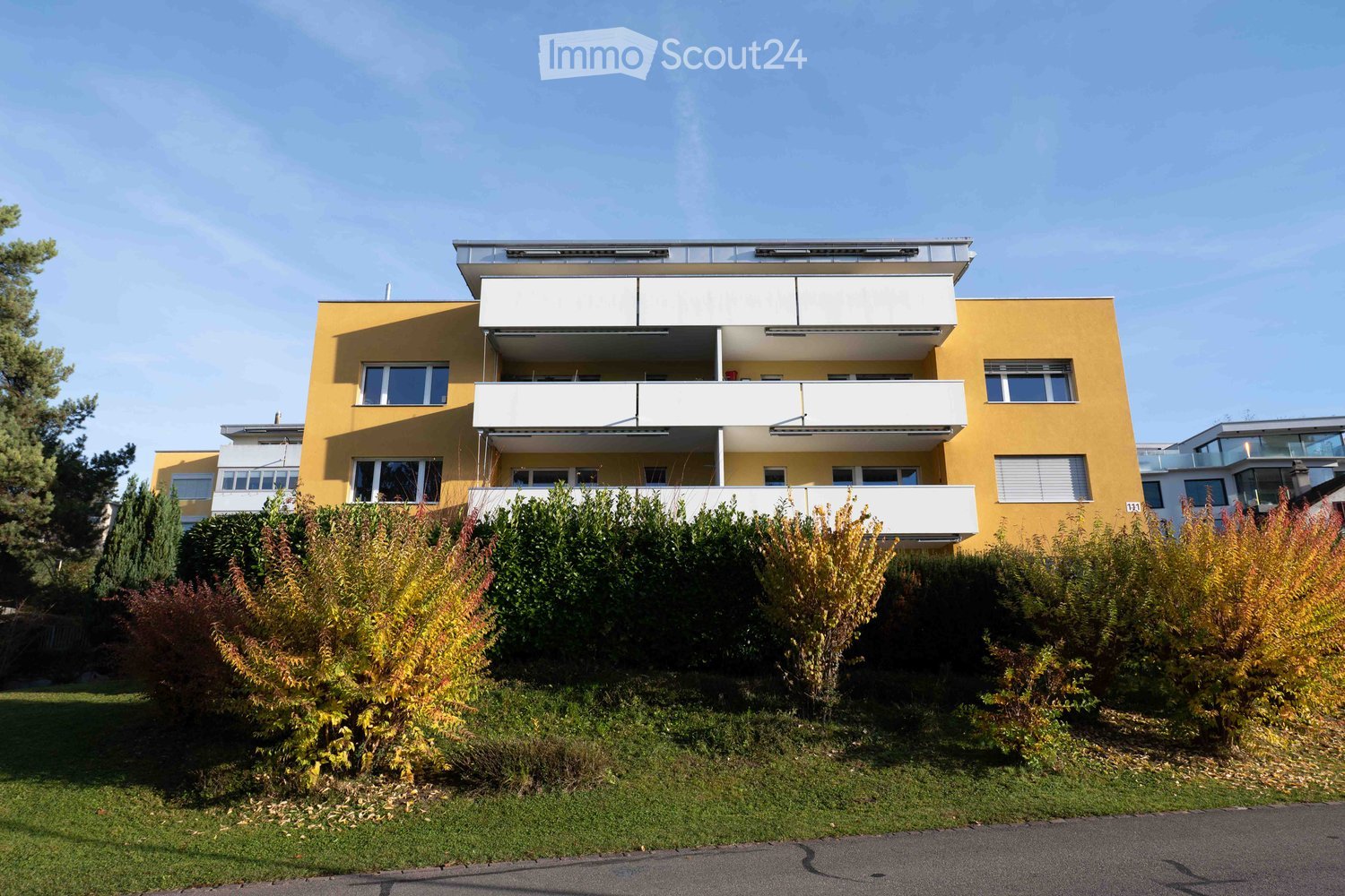 Yellow apartment building, several floors, balconies, glass windows, greenery below