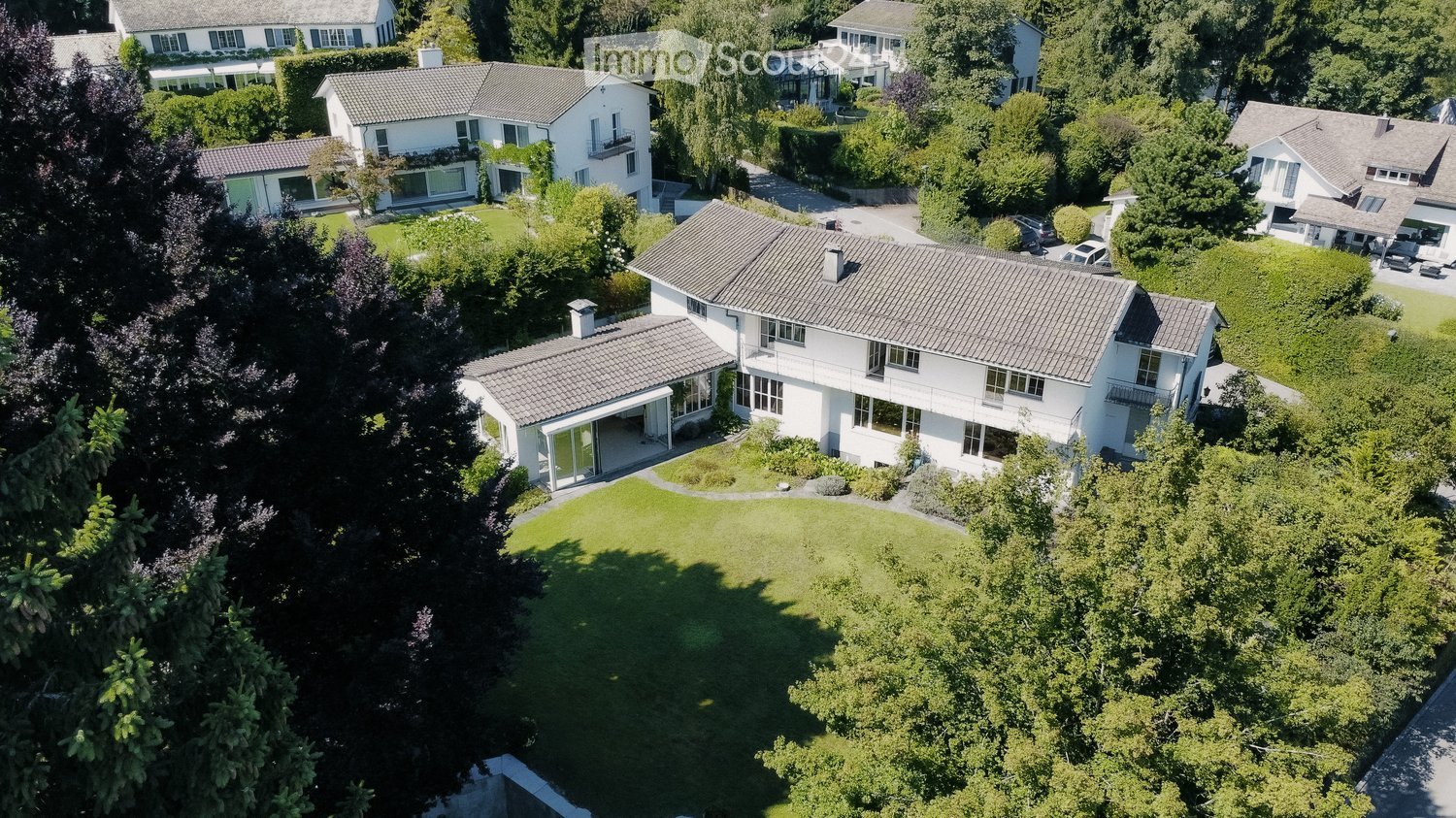 A large white house with a terrace, a driveway, and a green lawn