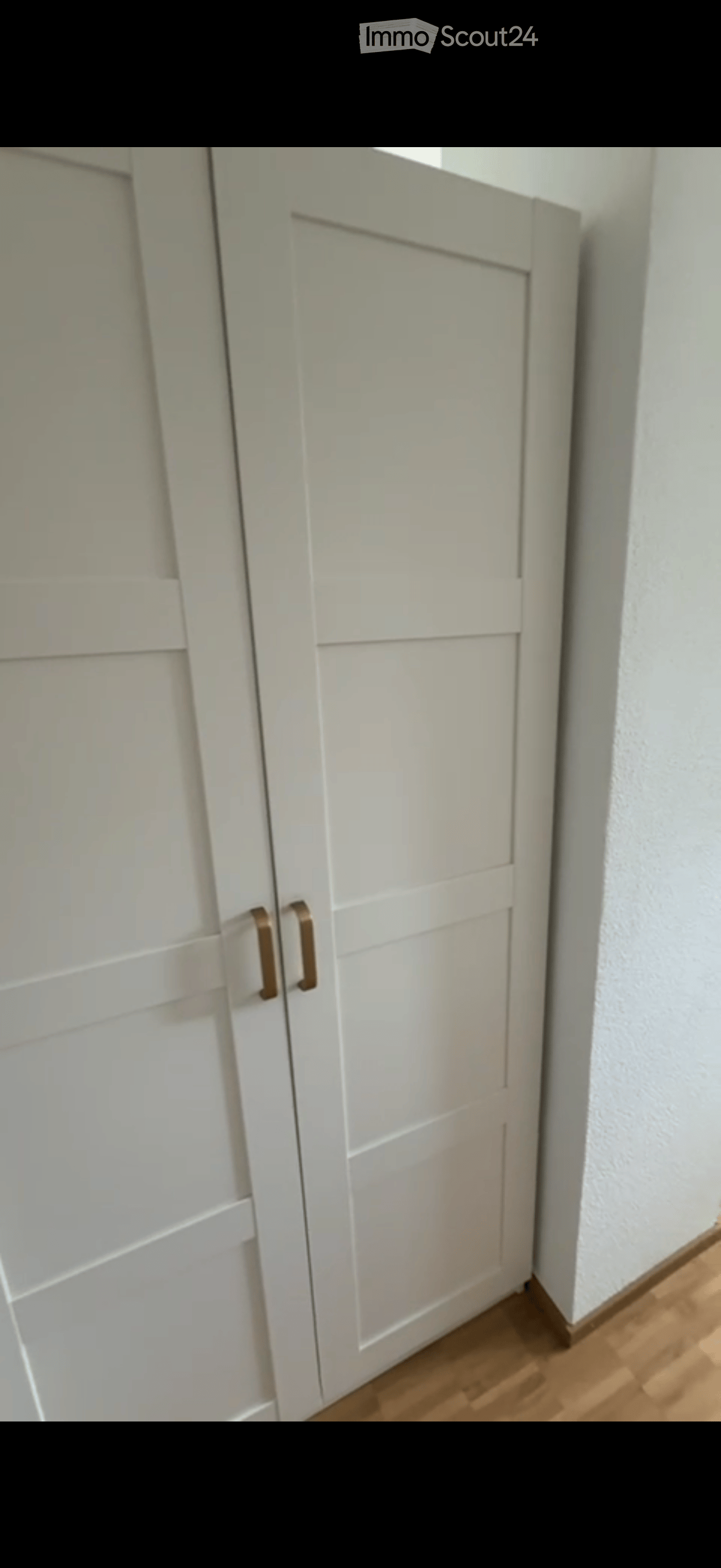 White double doors with horizontal panels and gold handles on a wooden floor next to a white wall.