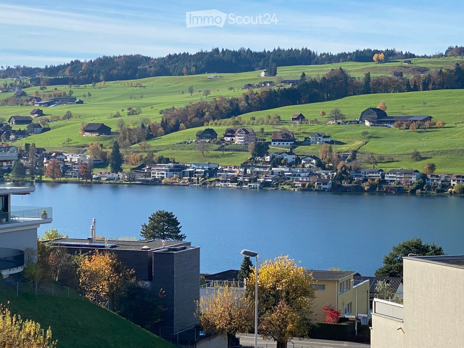 building with balcony on the left with a view of a lake and houses and hills