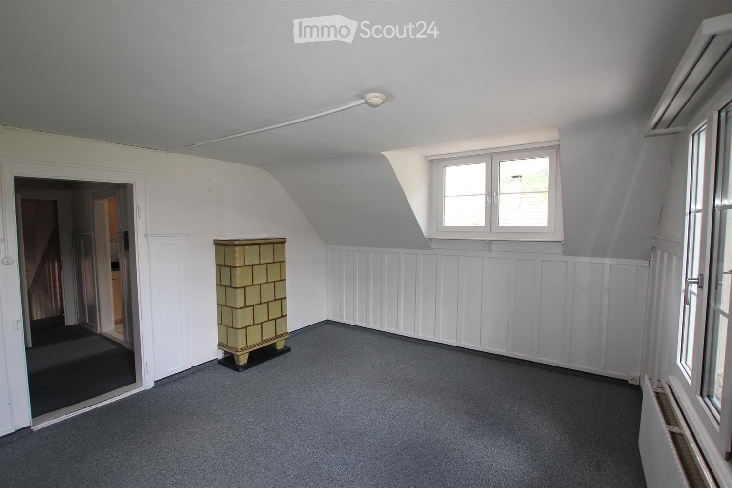 empty room, gray flooring, white walls, tiled stove, windows, door