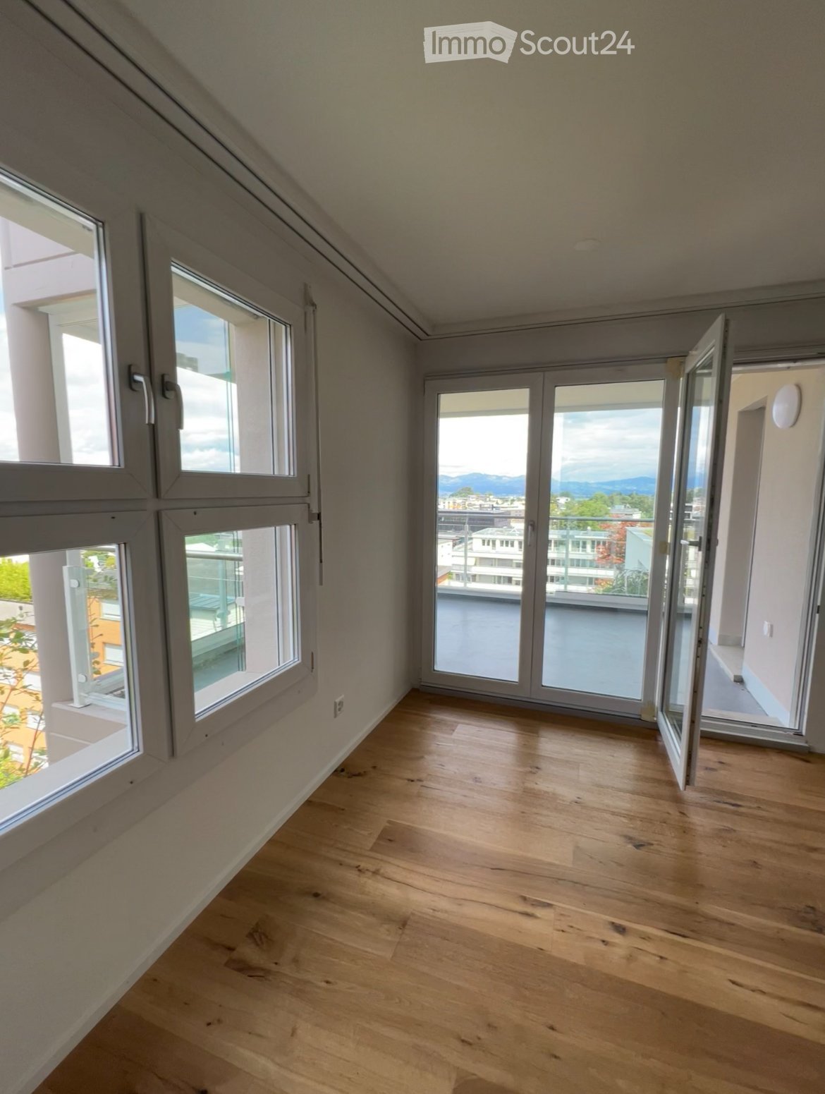 wooden floor, sliding doors leading to balcony, large windows, open doors, mountain view