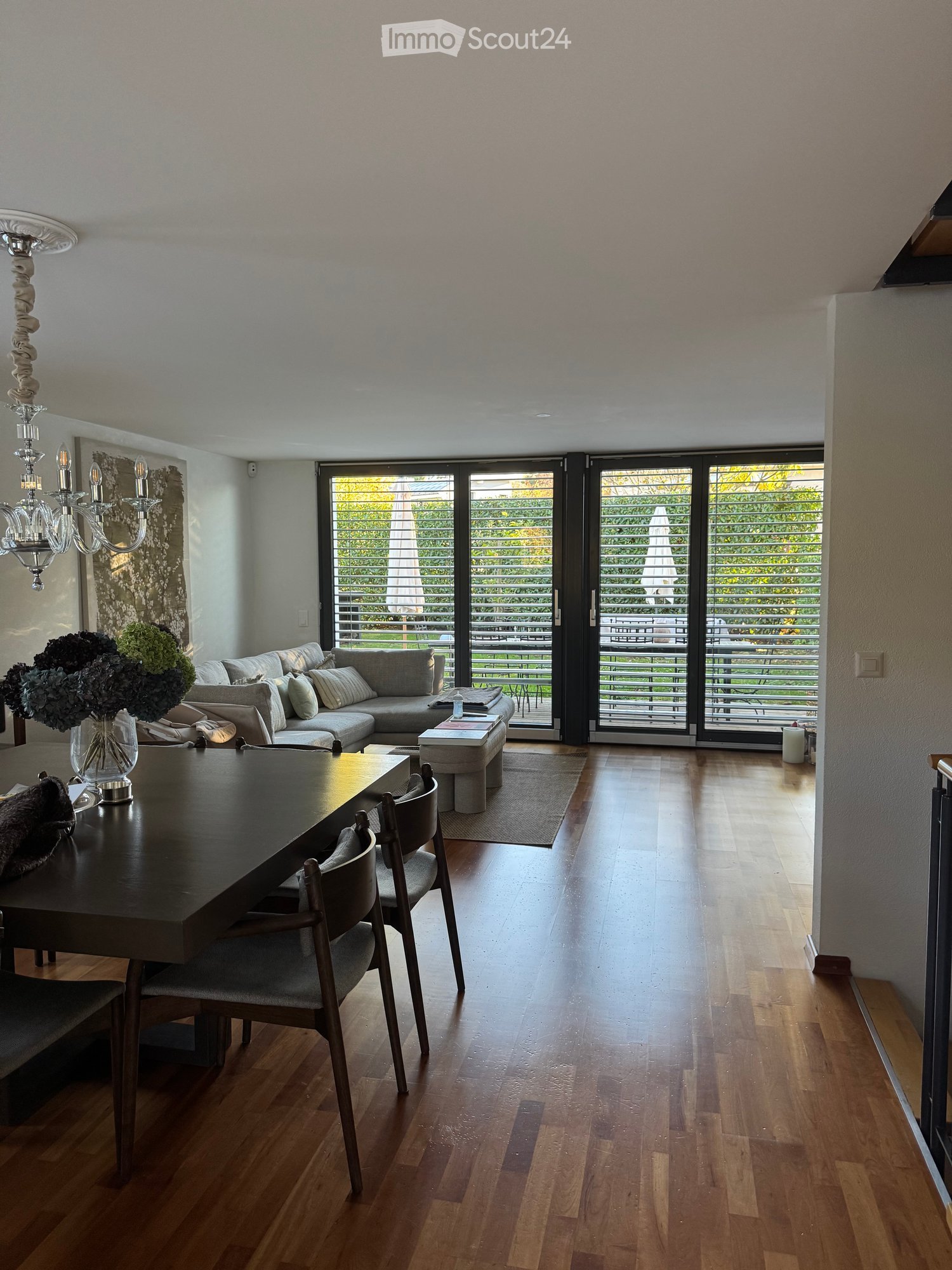 open living room with dining table and grey sofa, large glass sliding doors to balcony, hardwood floor, chandelier