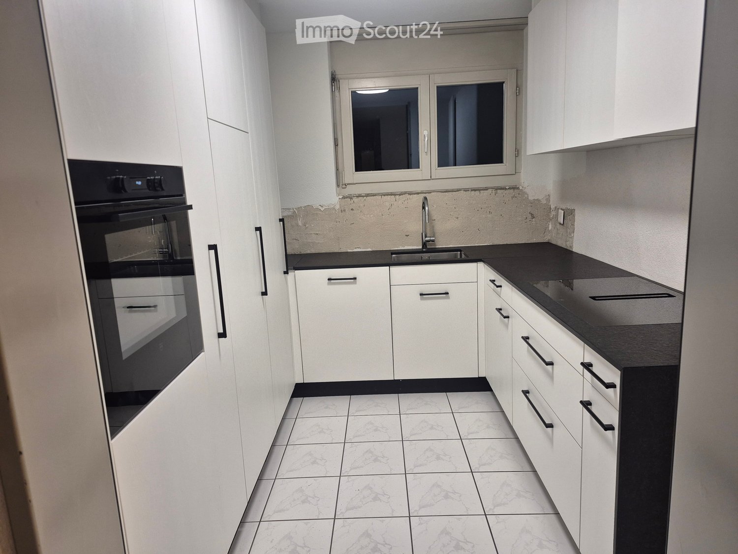modern kitchen with white cabinetry, black counter tops, integrated oven, sink, and faucet, tiled flooring, windows, and a power outlet
