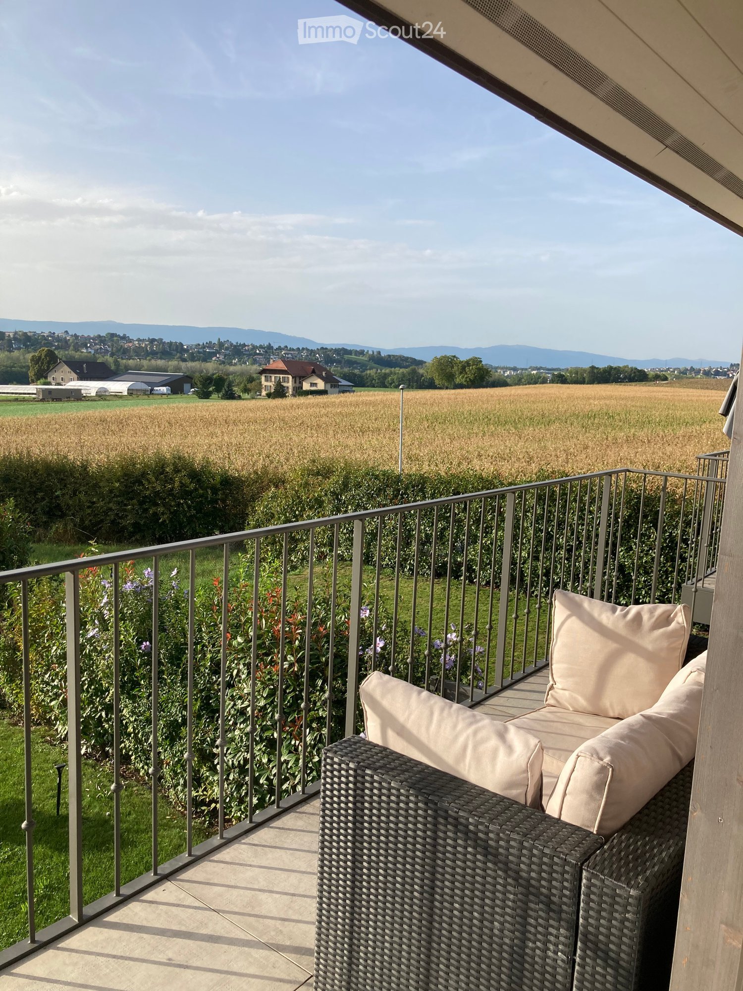 balcony, couch with pillows, metal railing, greenery, golden fields