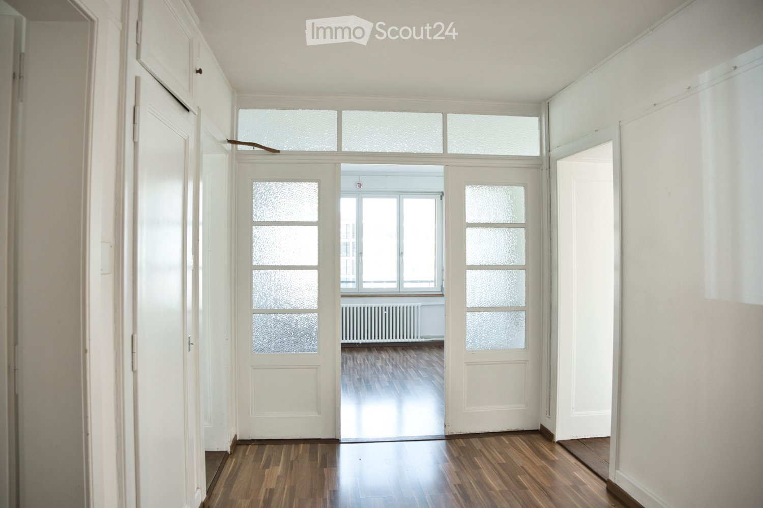 empty hallway with wooden floors, white doors, windows with glass panels