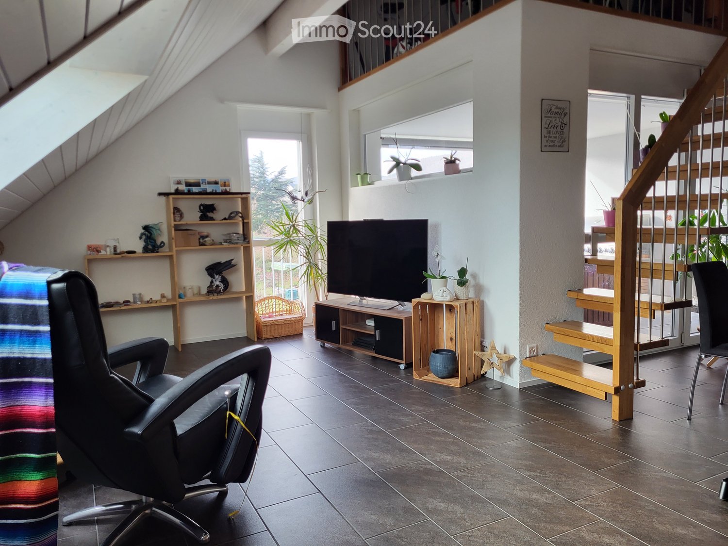 open floor plan, modern furniture, living room with sofa, chair, TV, entertainment center, shelves, stairs, potted plants, decorative items