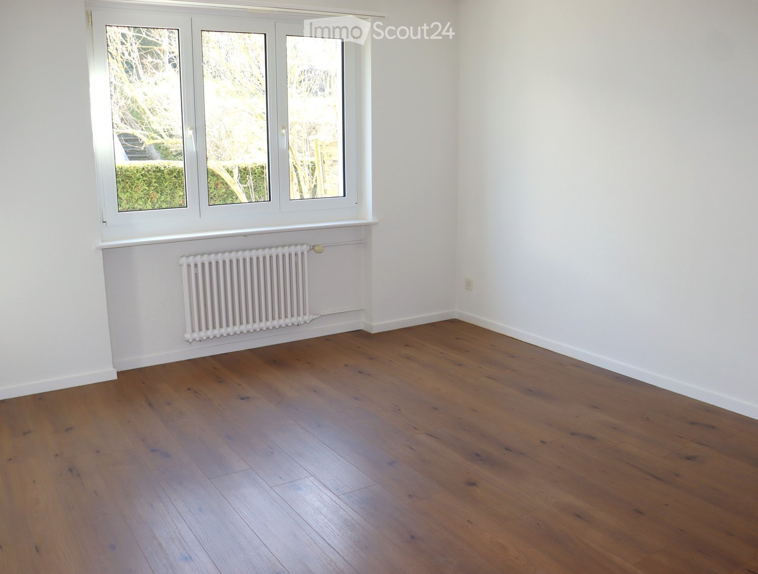 empty room with wooden floor, white walls, window, and radiator