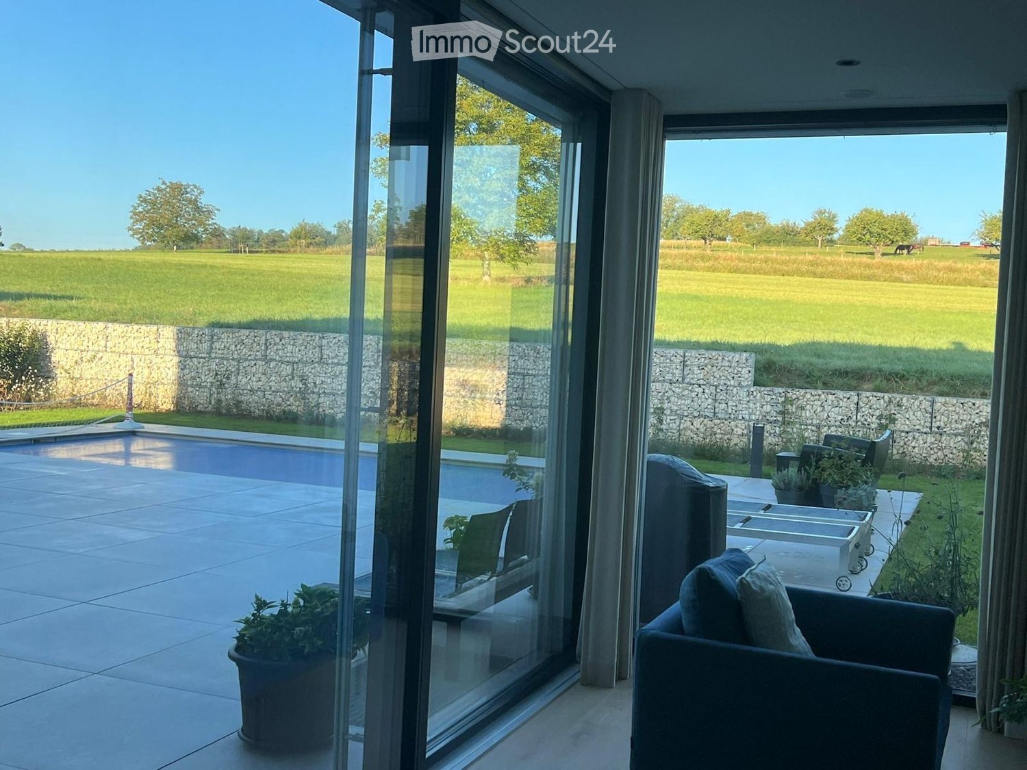 sliding doors, large windows, view of swimming pool and fields, beige floors, lounge chairs