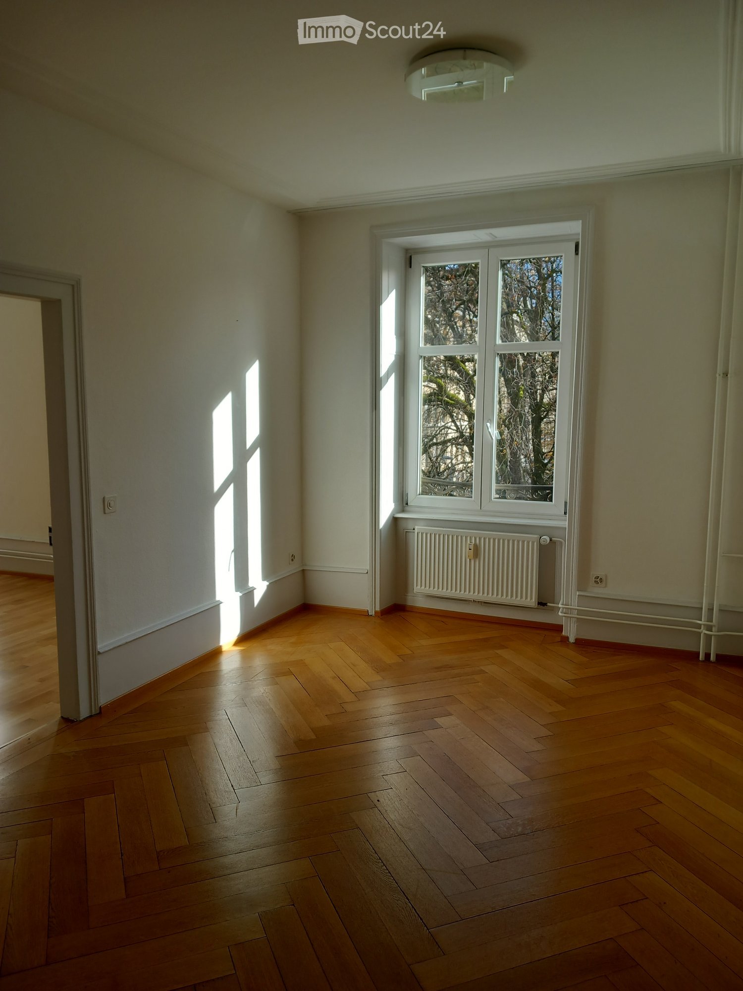 empty room, wooden floors, white walls, large window, radiator, small entrance