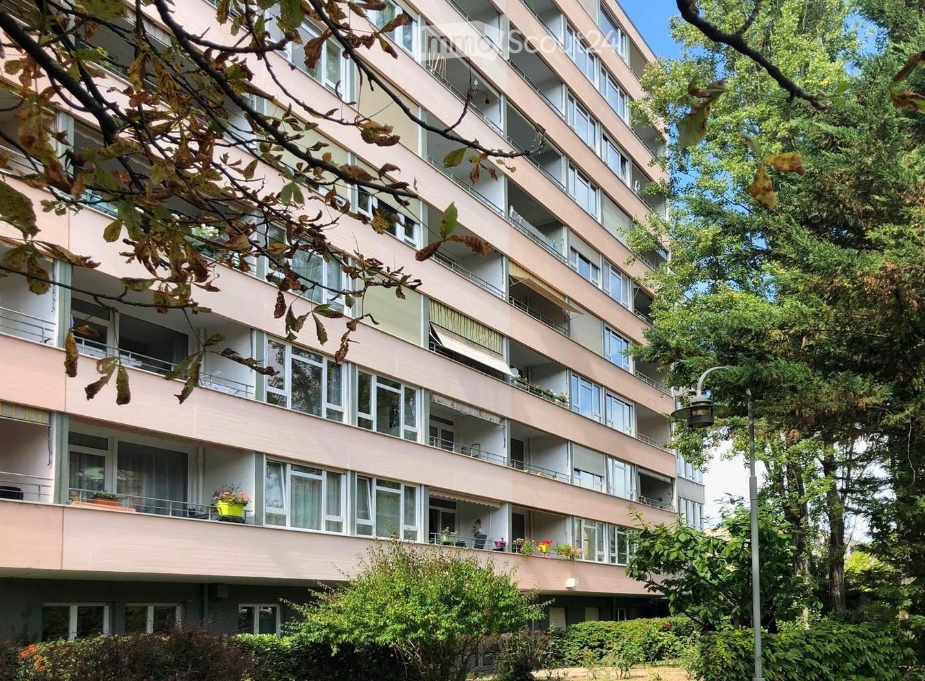 large apartment building with multiple balconies, multiple floors, greenery in the front