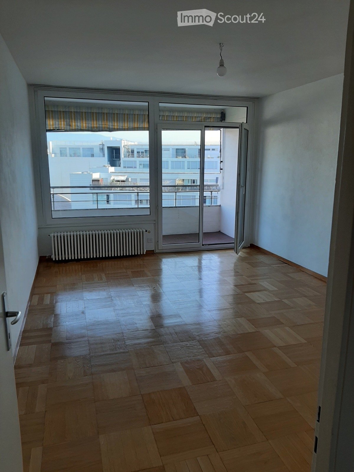 Empty room, wooden parquet floor, large windows, balcony with railing, ceiling light