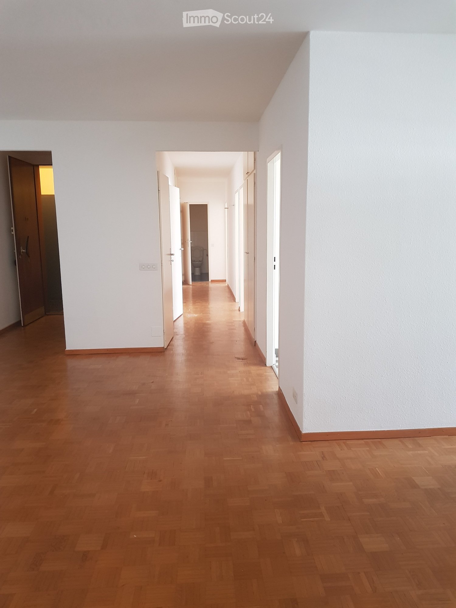 wooden floors, white walls, open doors leading to other rooms, hallway lighting