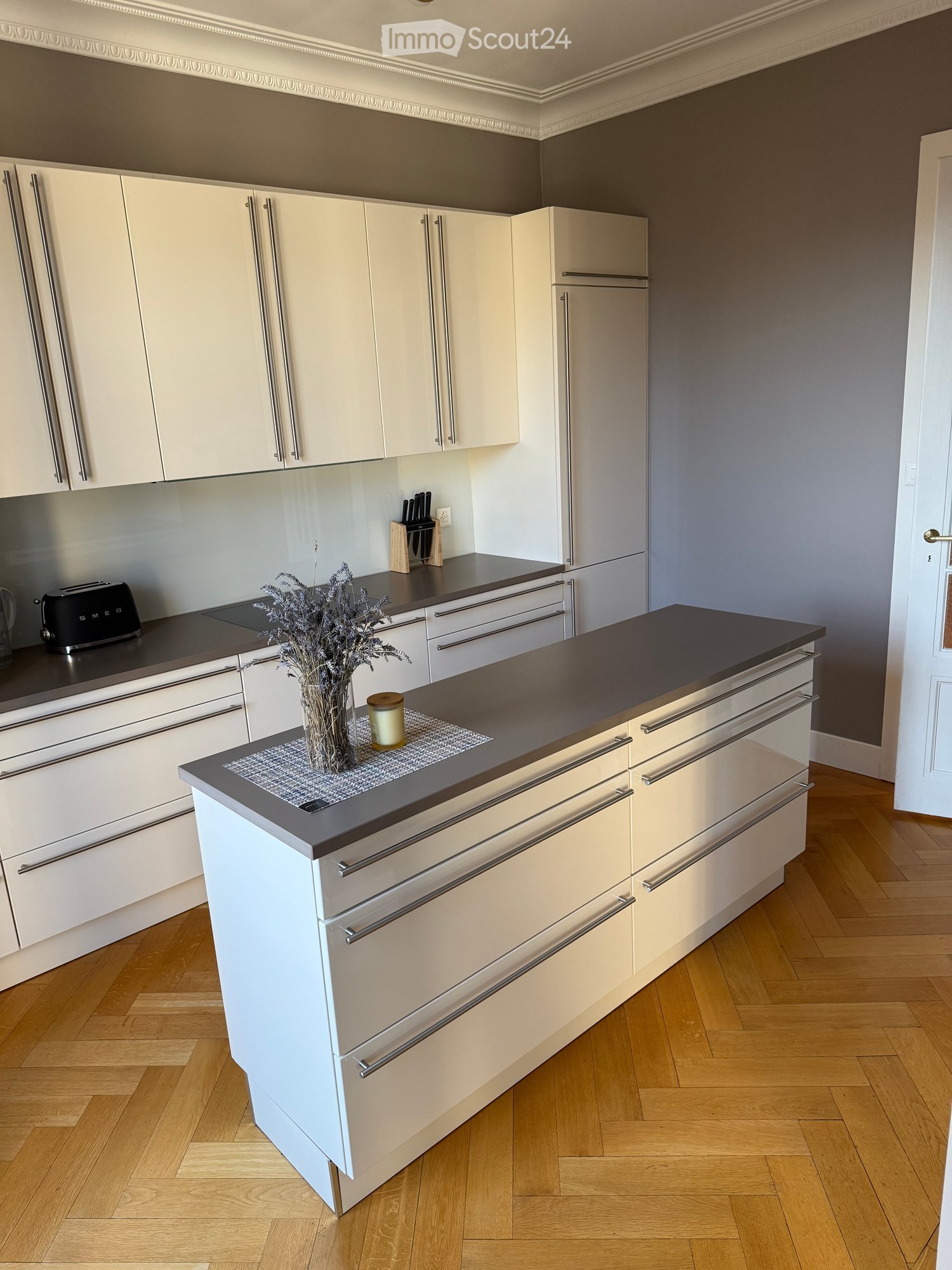 Modern kitchen with white cabinets, wooden flooring, central island, gray countertops, and integrated refrigerator.