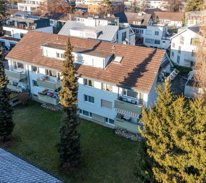 An apartment building with brown roofs, balconies, and green lawn with trees.