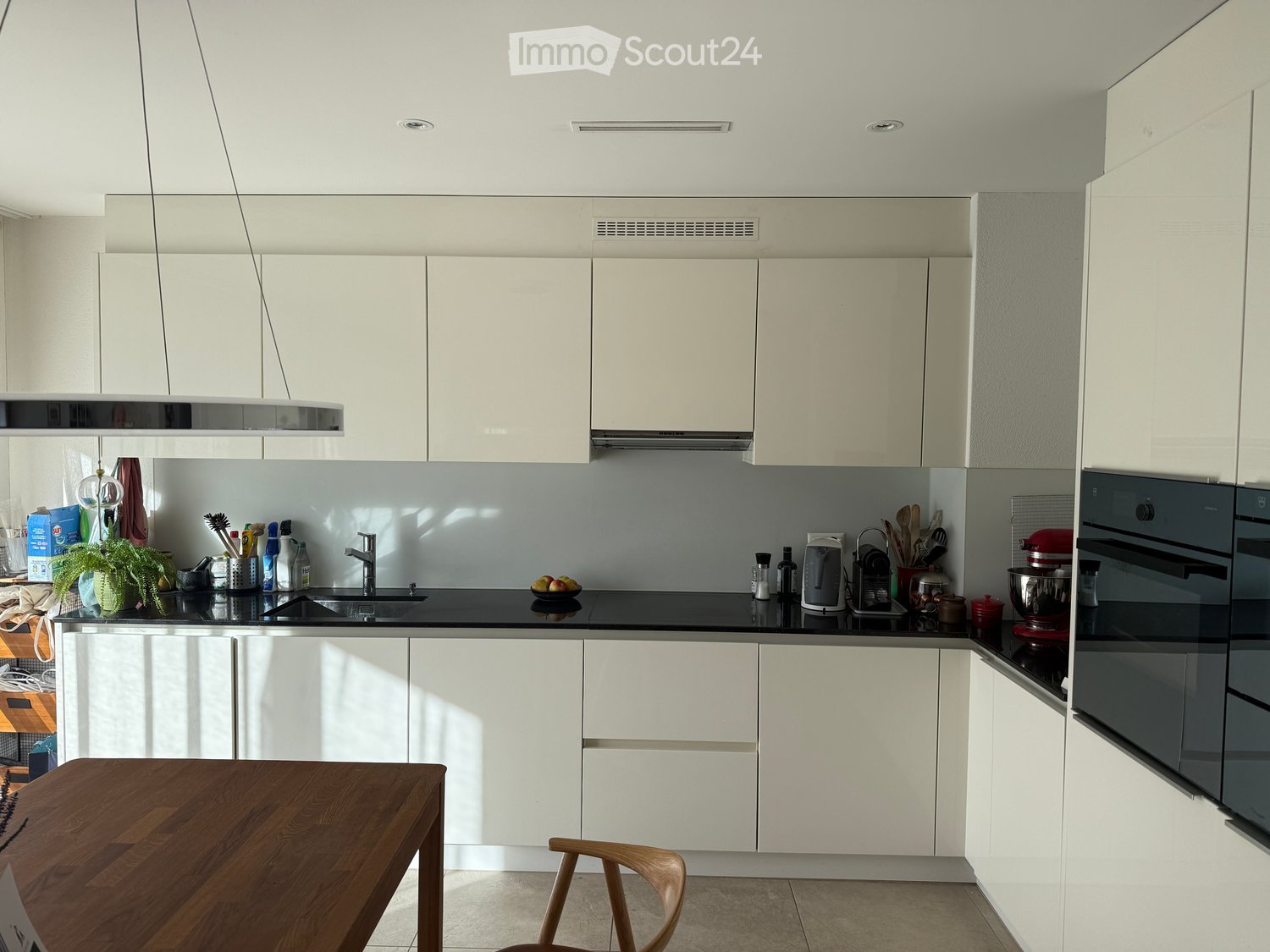 modern kitchen with white cabinets, black countertops, stainless steel appliances, and wooden dining table