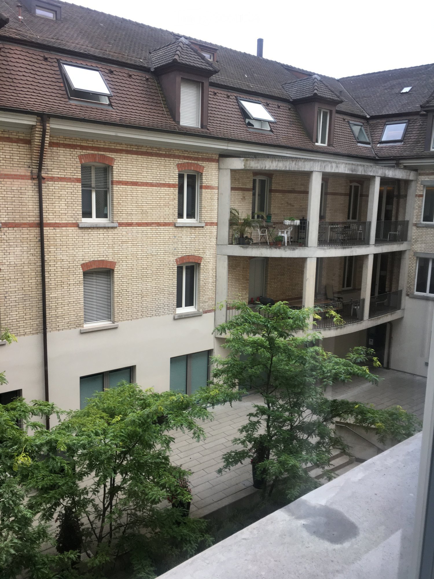 5 story building, balcony on 4th floor, brick facade, double glass windows, outdoor plants