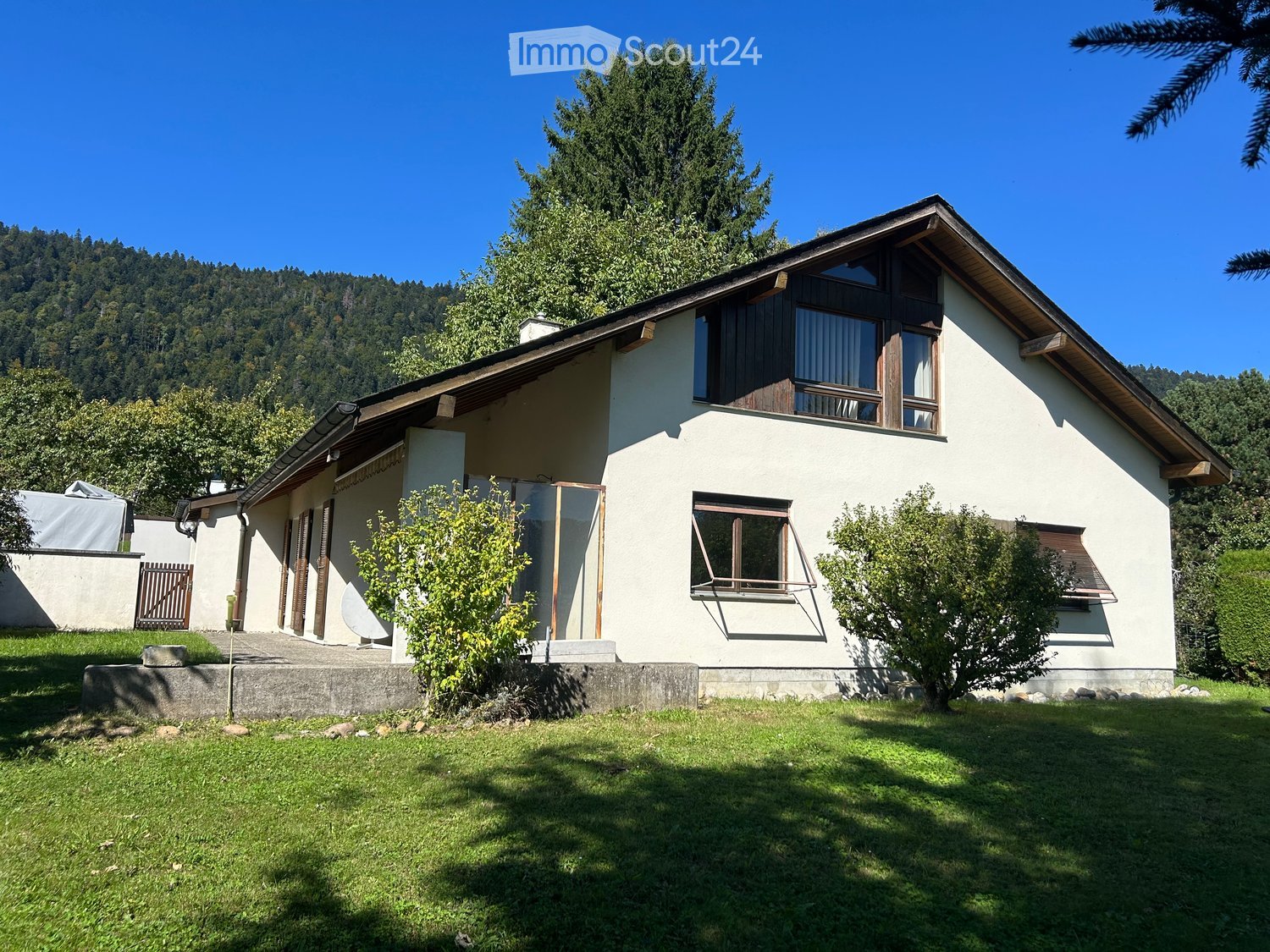 1 story house, white paint, brown roof, balcony, garden, trees in the background
