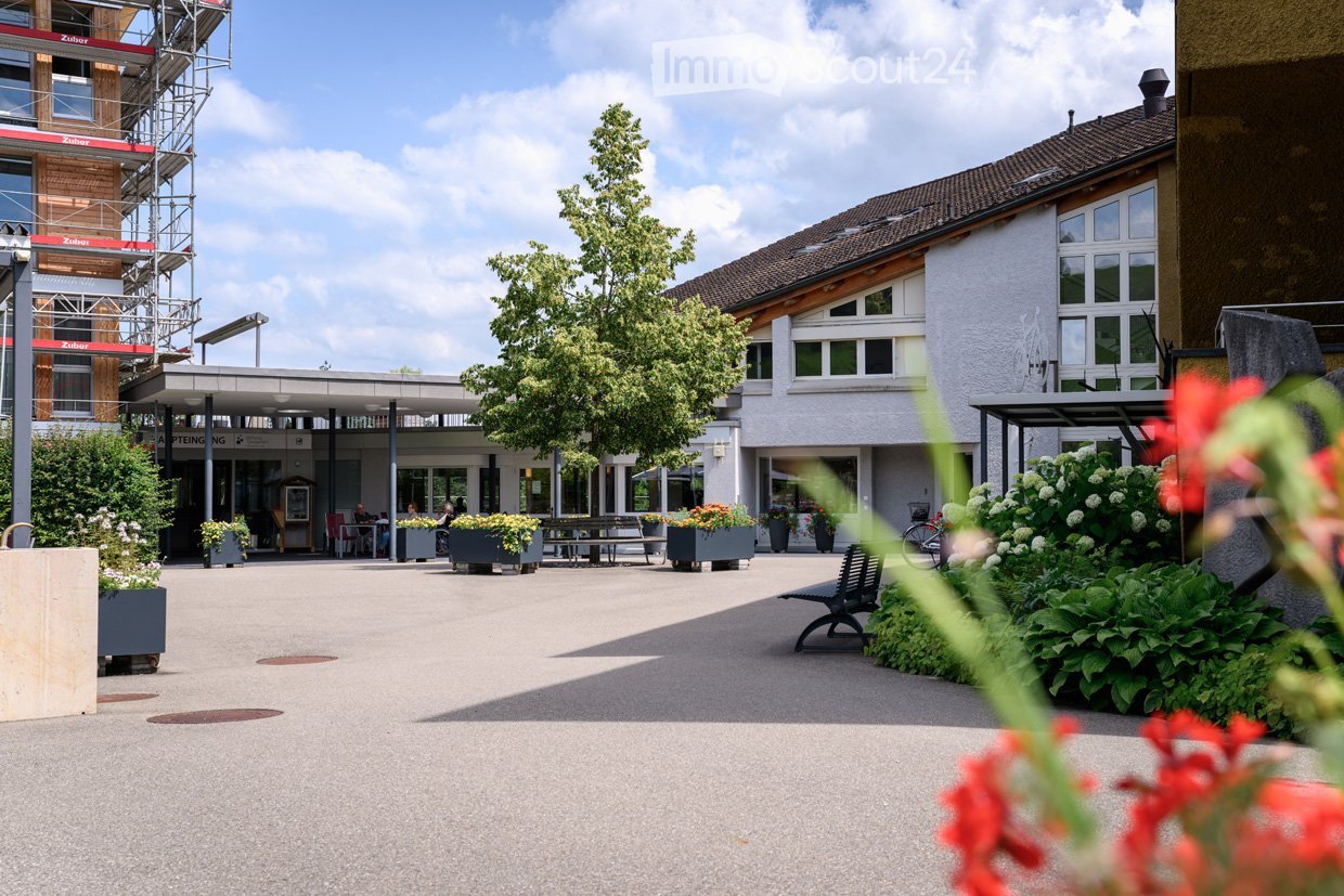 white exterior, multiple windows, entrance with benches, garden with benches and tables, tree, paving