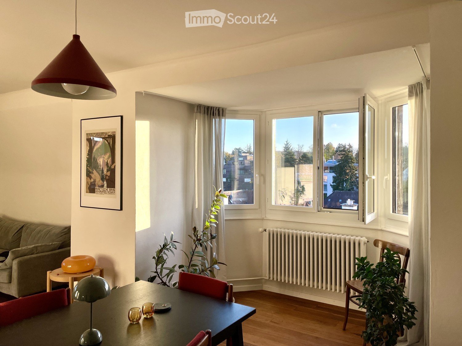dining room with dining table, chairs, radiator, two plants, windows, picture, lamp, couch, orange bowl