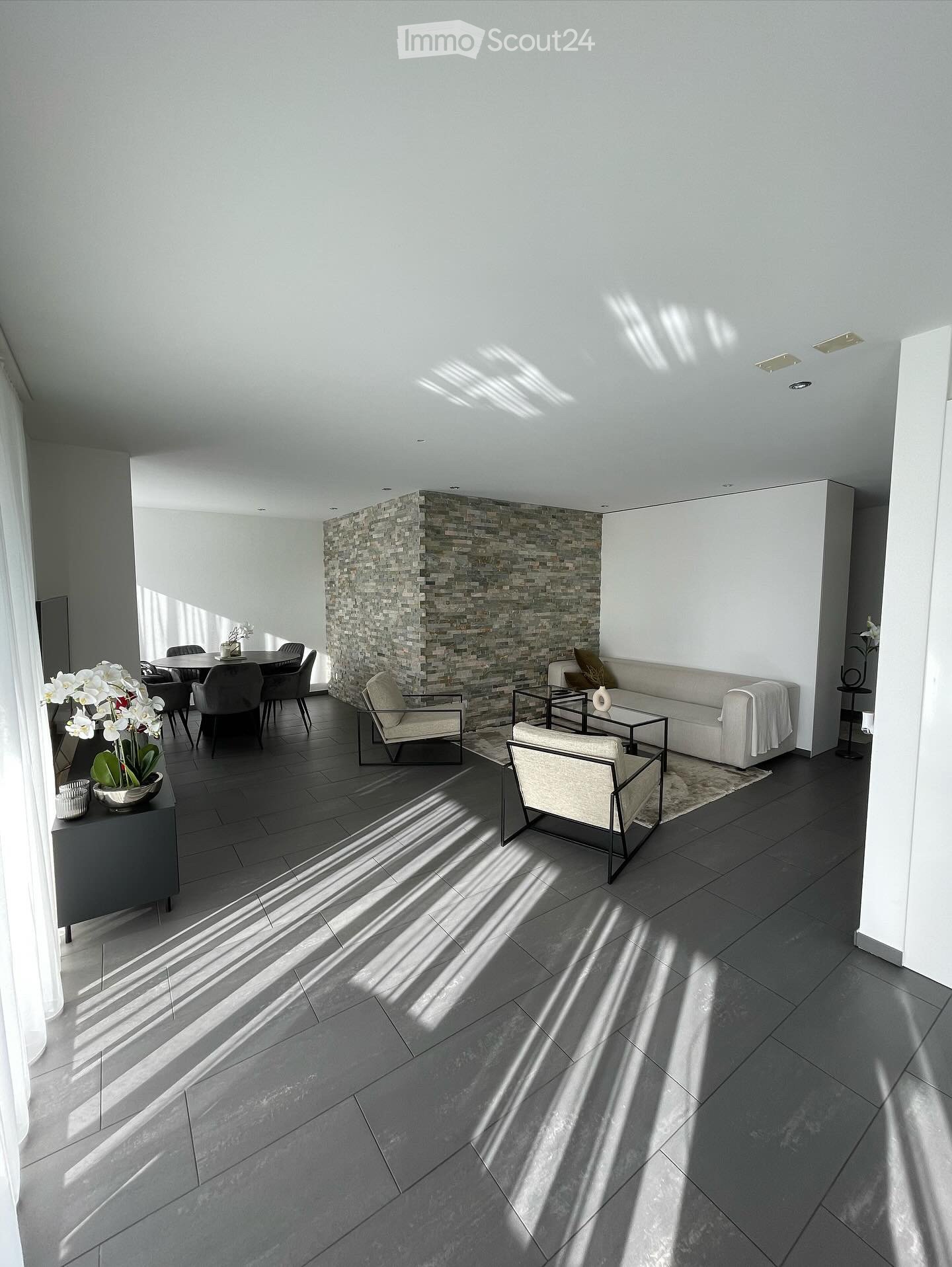 open-plan living room with stone wall, white furnishings, and white tiled floor