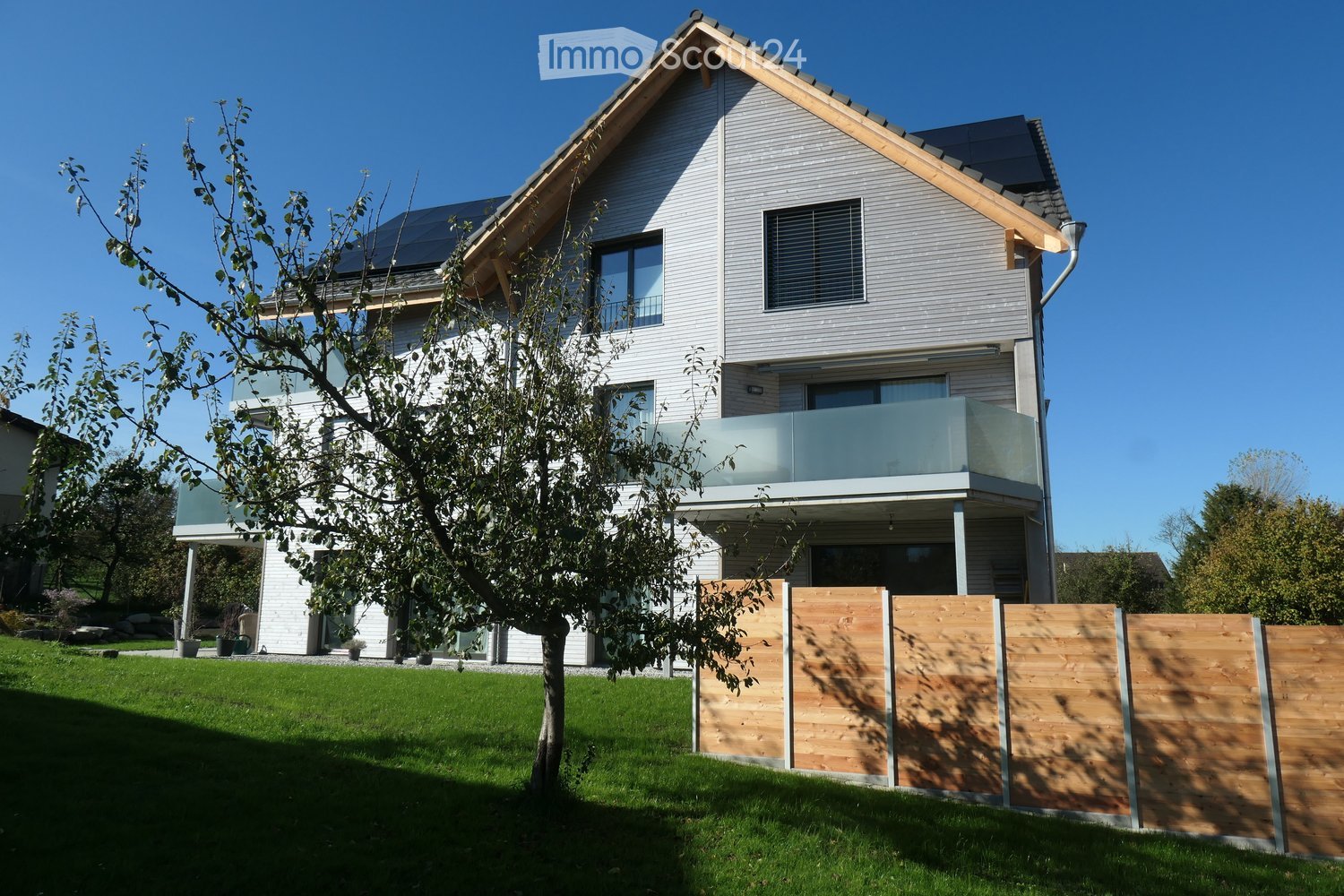 2 story house, white exterior, solar panels on the roof, glass balcony, wooden fence