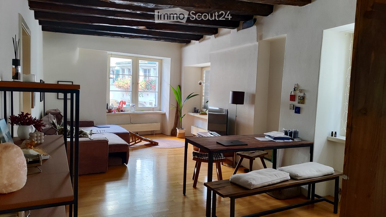 living room with sofa, desk, table with books, wooden floor, couch, potted plant, radiator