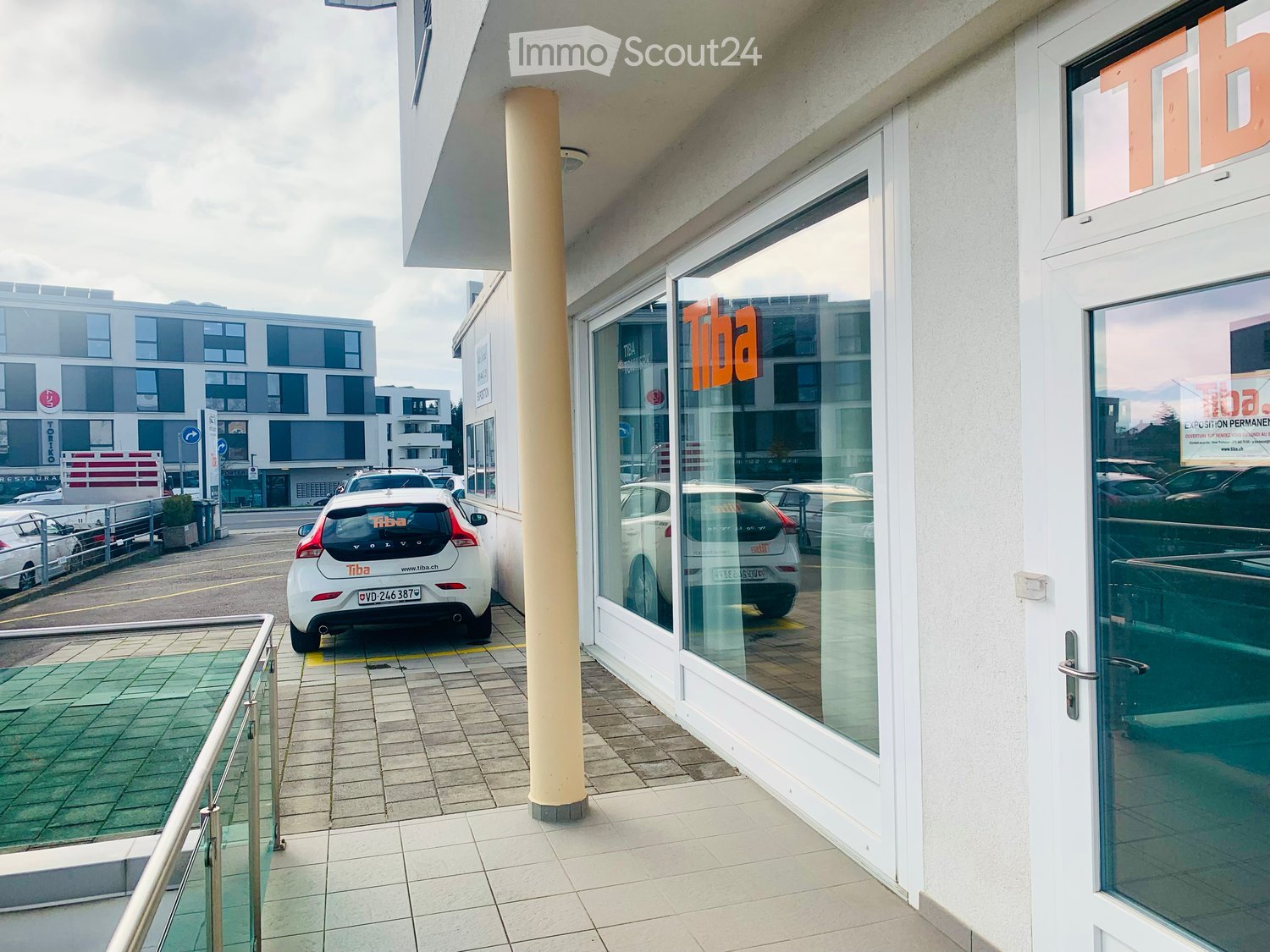 Entrance of building, parking space, multiple cars parked in the background