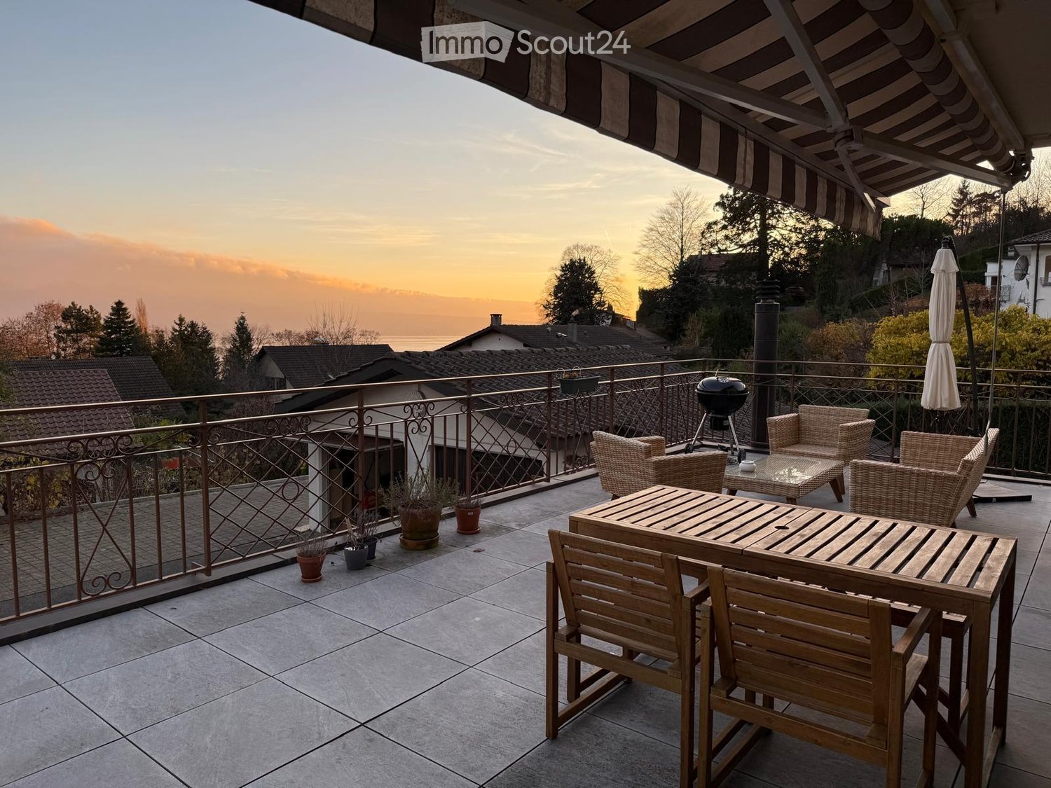 Terrace with table, chairs, metal railing, BBQ grill, umbrellas, potted plants, and scenic view of the landscape