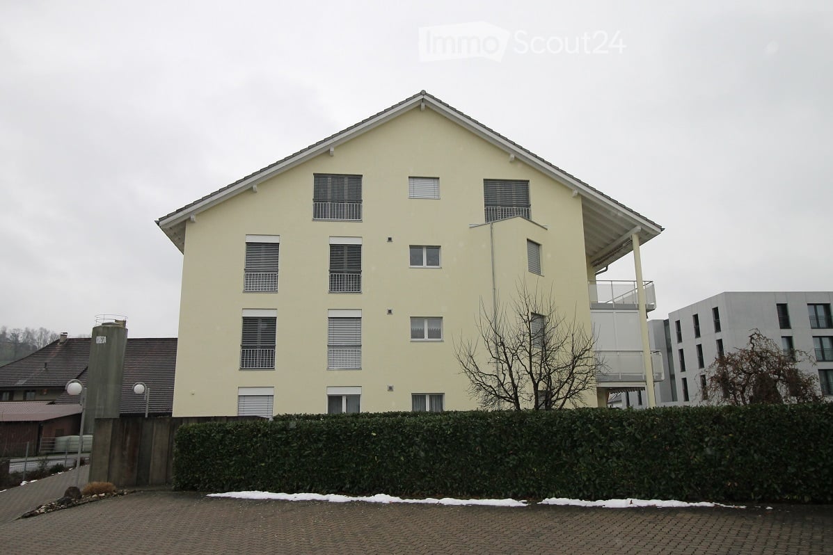 two-story building, yellow walls, multiple windows, balconies on multiple floors, hedges in front