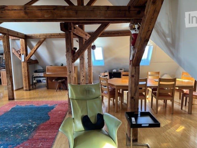 Dining area with dining table, wooden beams, rug, green chair, piano, wooden dining chairs