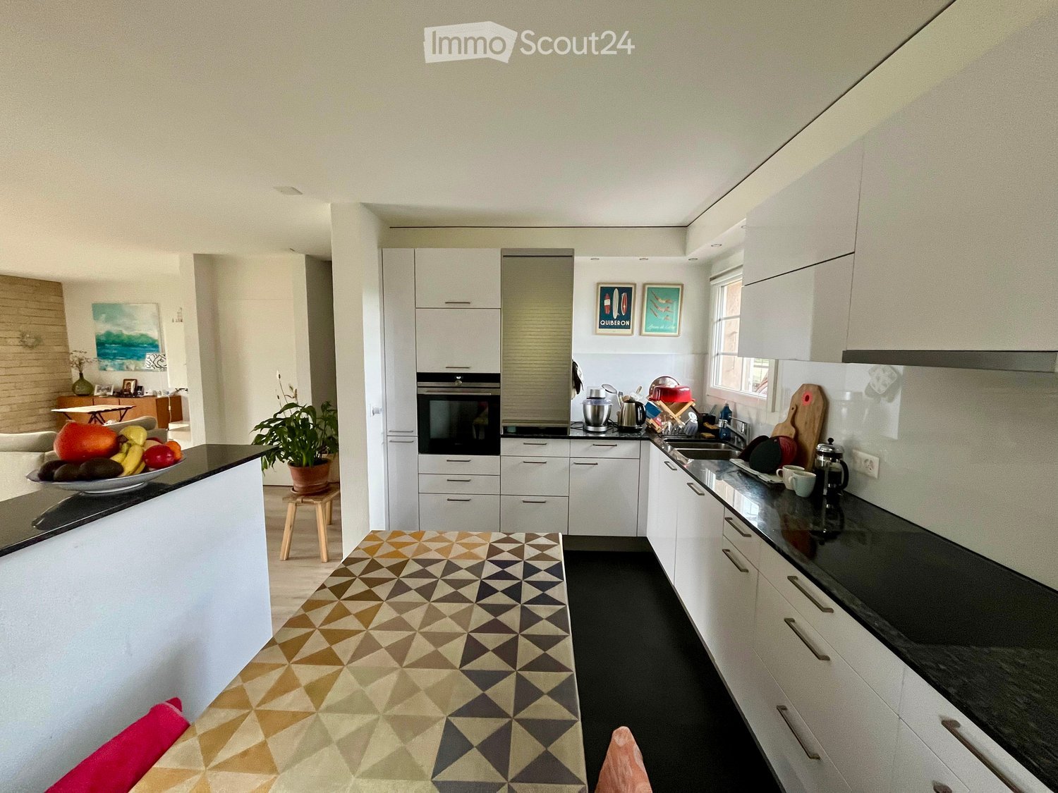 white cabinets, black countertops, white walls, kitchen island, stainless steel appliances, window, picture frames, chopping board, potted plant, table