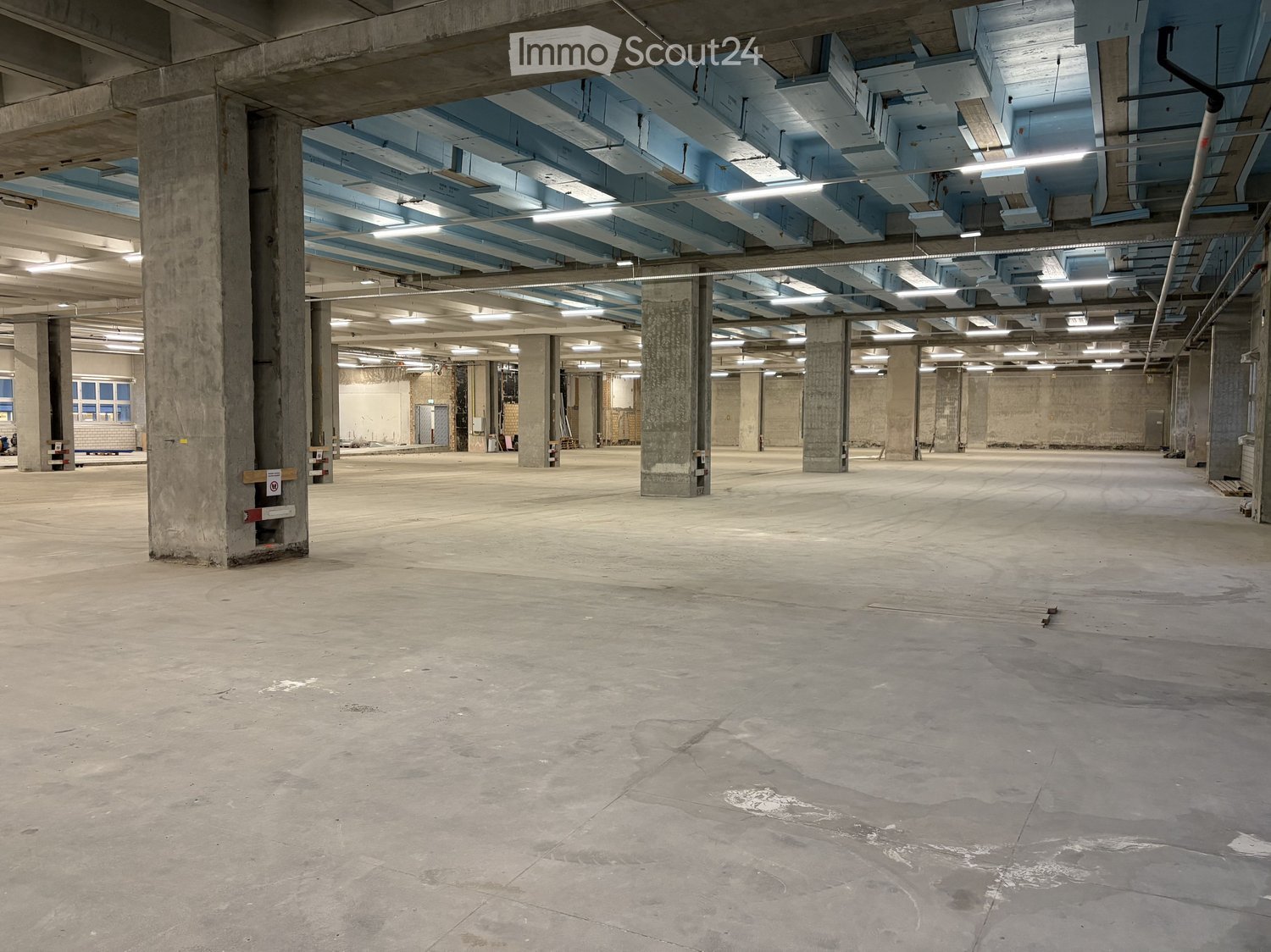 empty room with concrete pillars and blue beams, large open space, unfinished ceiling with exposed pipes and lighting